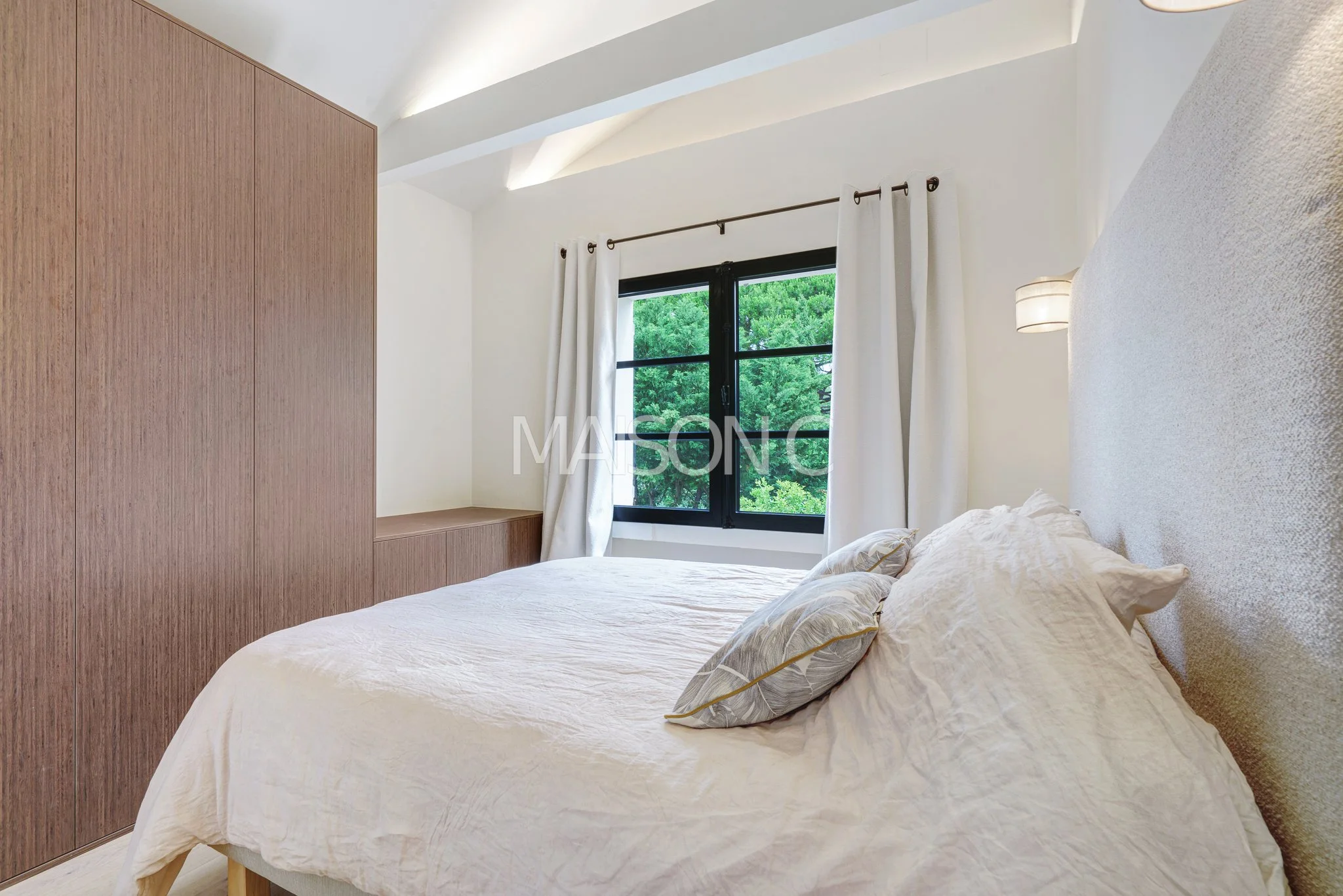 Chambre moderne avec lit double, fenêtre avec vue sur des arbres, murs blancs, placard en bois foncé, rideaux blancs, éclairage doux.