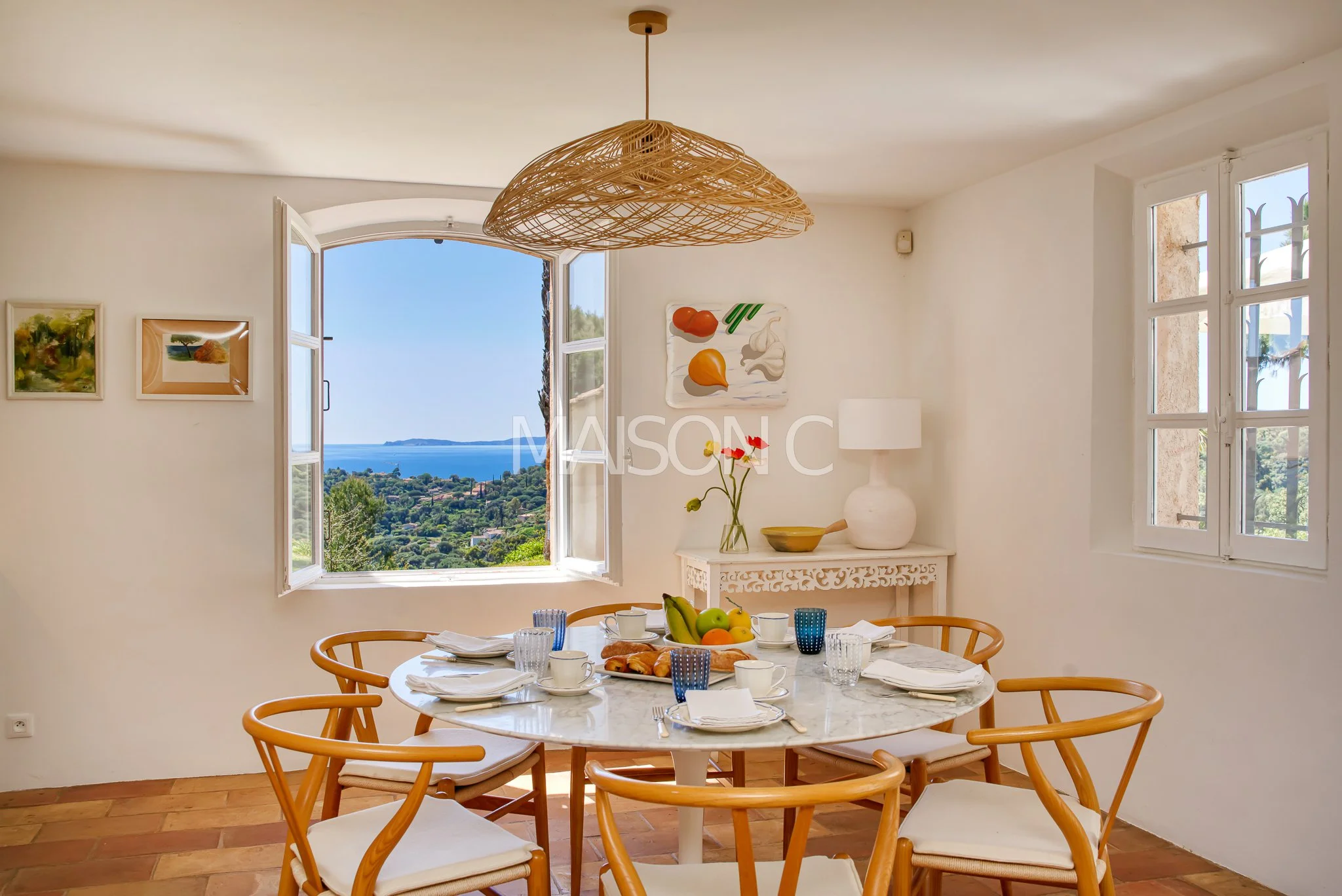 Salle à manger avec table ronde, chaises en bois, petit déjeuner, fenêtres ouvertes, vue sur la mer