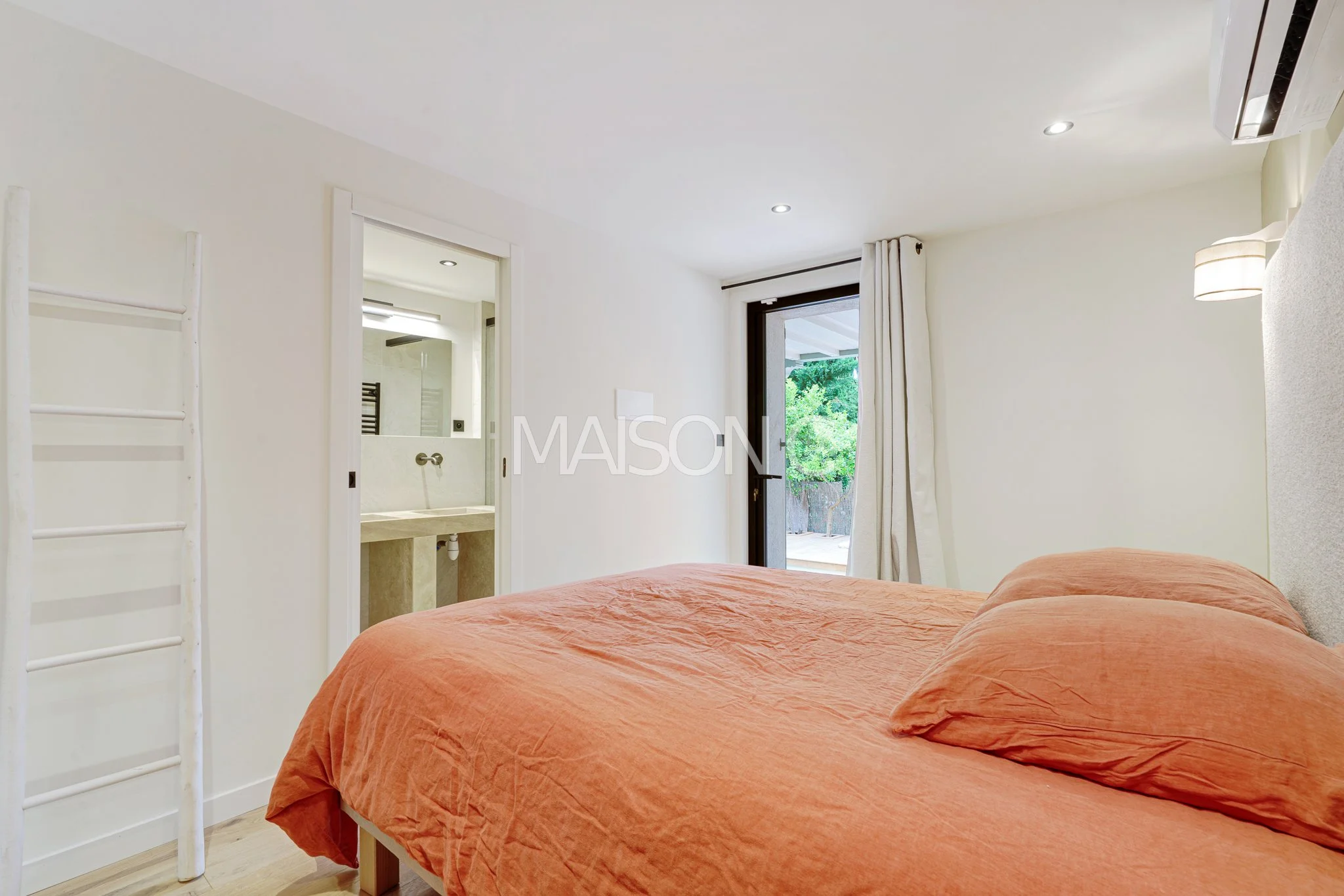 Chambre chaleureuse avec lit orange, porte-fenêtre donnant sur une terrasse, petite salle de bain attenante visible à gauche