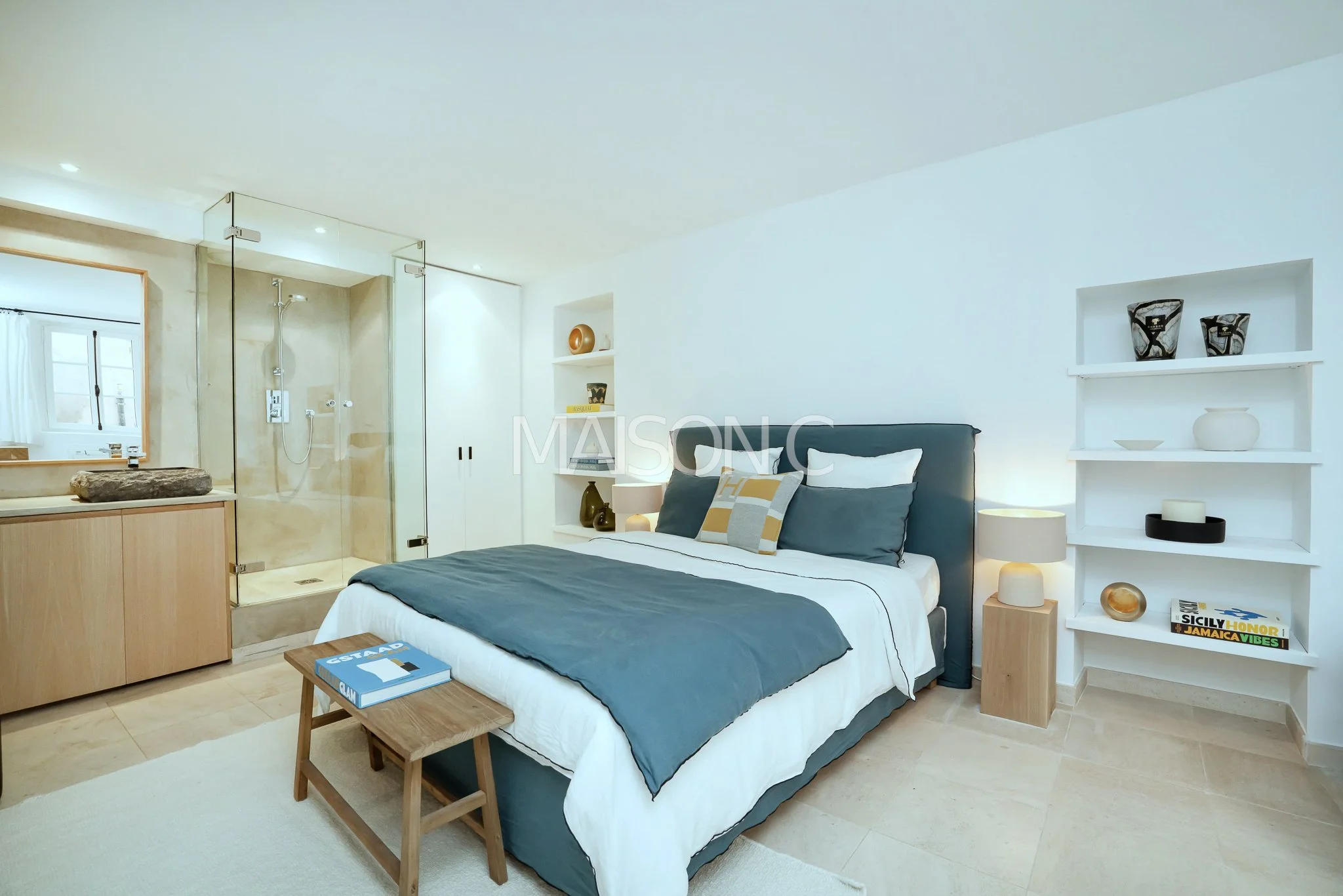 Chambre avec lit double, coussins et moquette, étagères blanches avec décorations, salle de bain attenante avec douche privée.