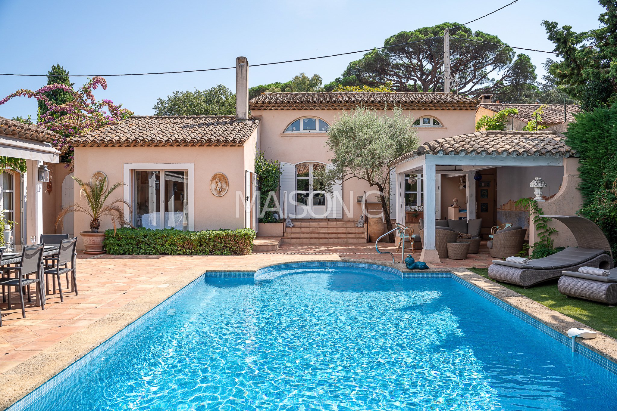 Maison méditerranéenne avec piscine, terrasse, mobilier d'extérieur et végétation luxuriante sous ciel dégagé.