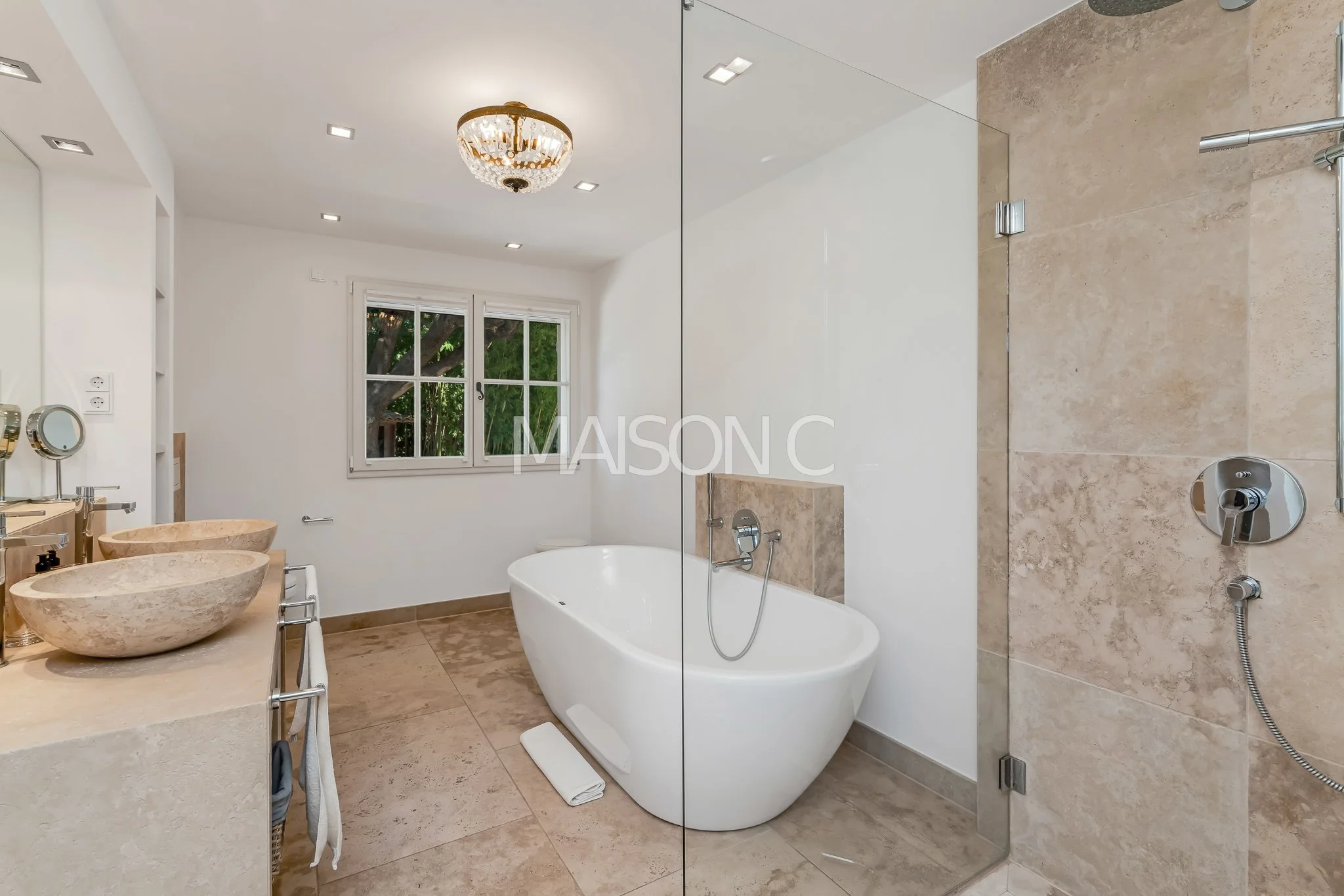 Salle de bain moderne avec baignoire autoportante, double vasques en pierre, douche à l'italienne et fenêtre donnant sur un jardin.