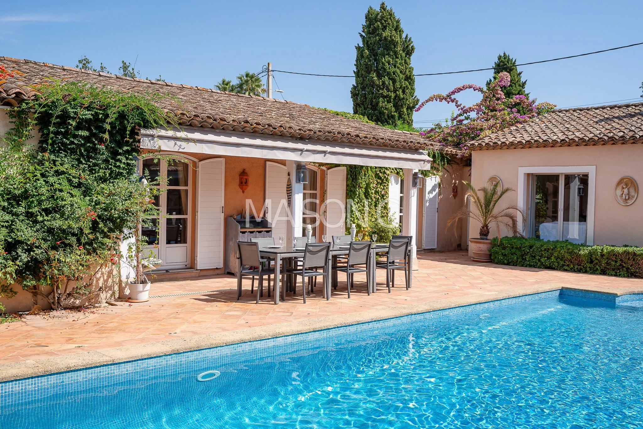 Courtyard with swimming pool, outdoor dining table, and surrounding greenery in a sunny, Mediterranean-style home.