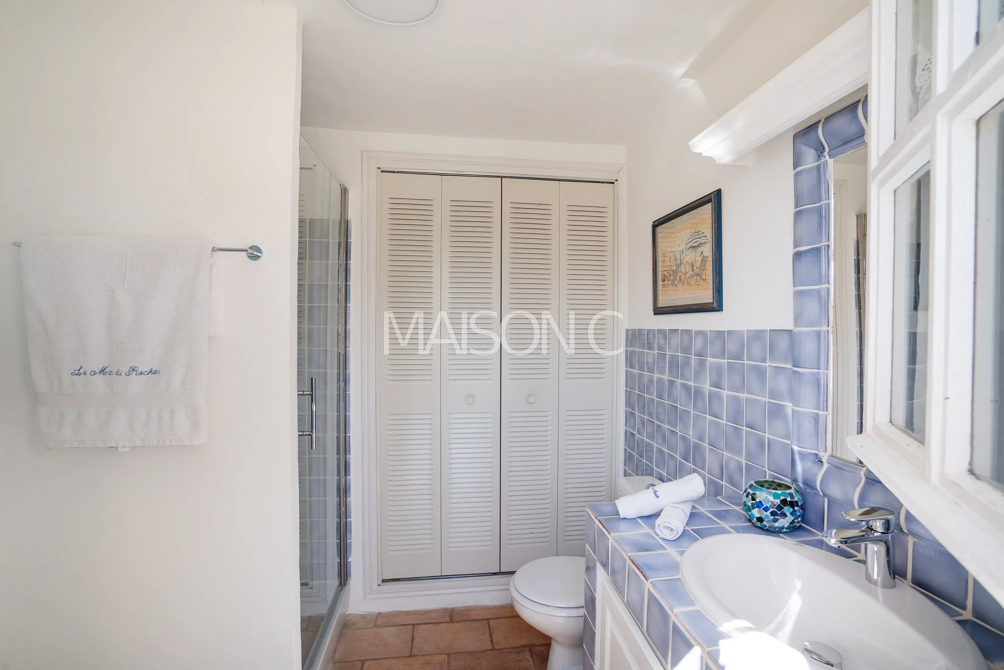 Salle de bain avec lavabo en mosaïque bleue, miroir, toilette et porte de placard en lamelles blanches.