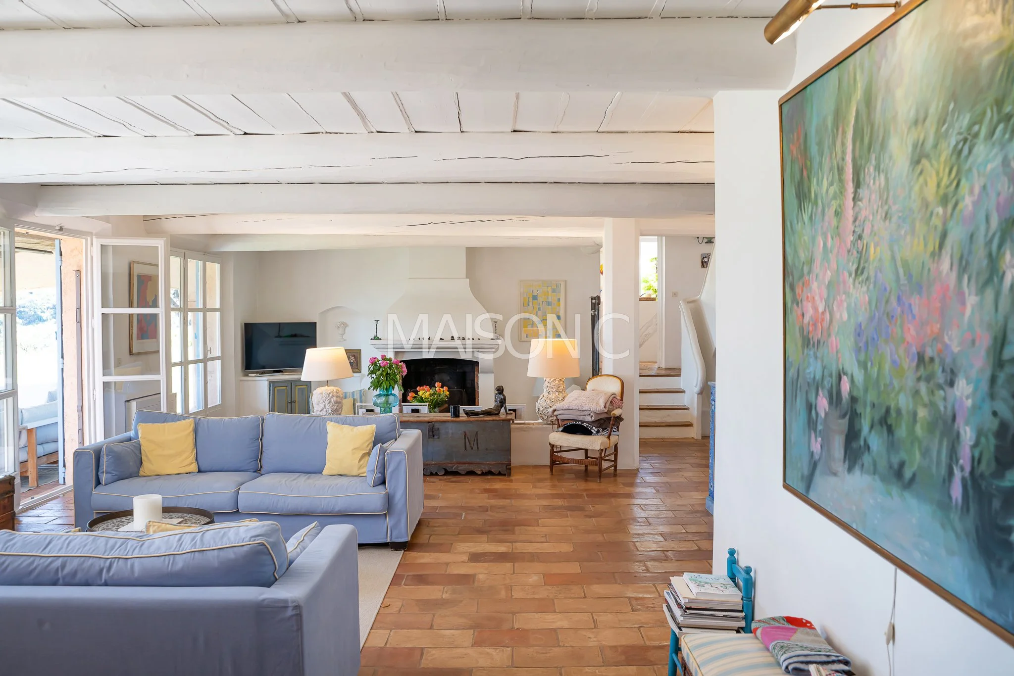 Intérieur d'un salon lumineux avec des canapés bleus, une cheminée blanche, une télévision, et des œuvres d'art accrochées aux murs.