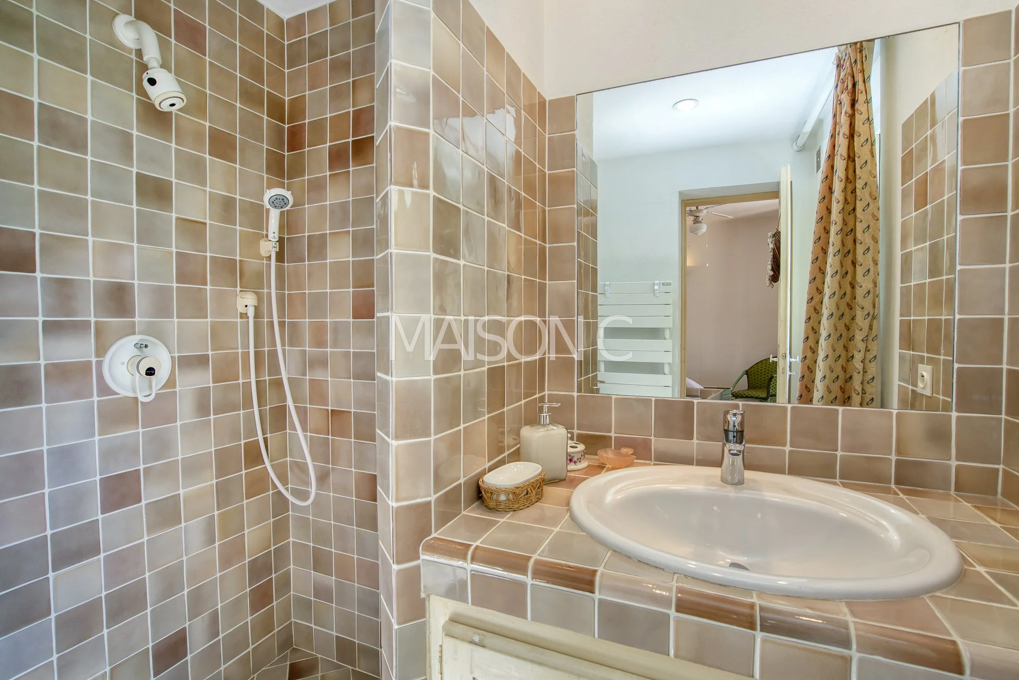 Salle de bain avec mosaïque beige, lavabo, miroir, et cabine de douche.