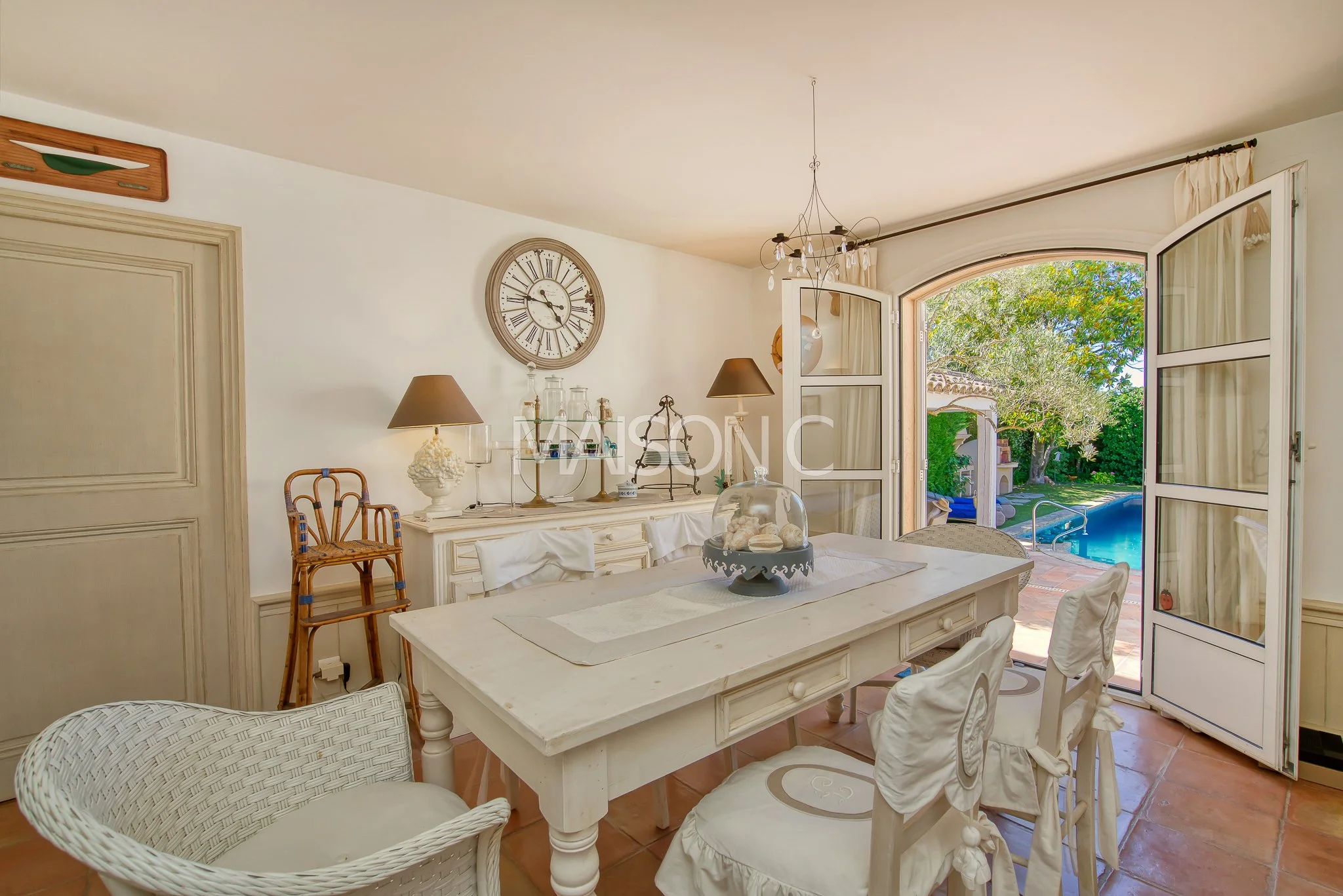 Salle à manger lumineuse avec table blanche, chaises et vue sur la piscine extérieure par une porte-fenêtre ouverte