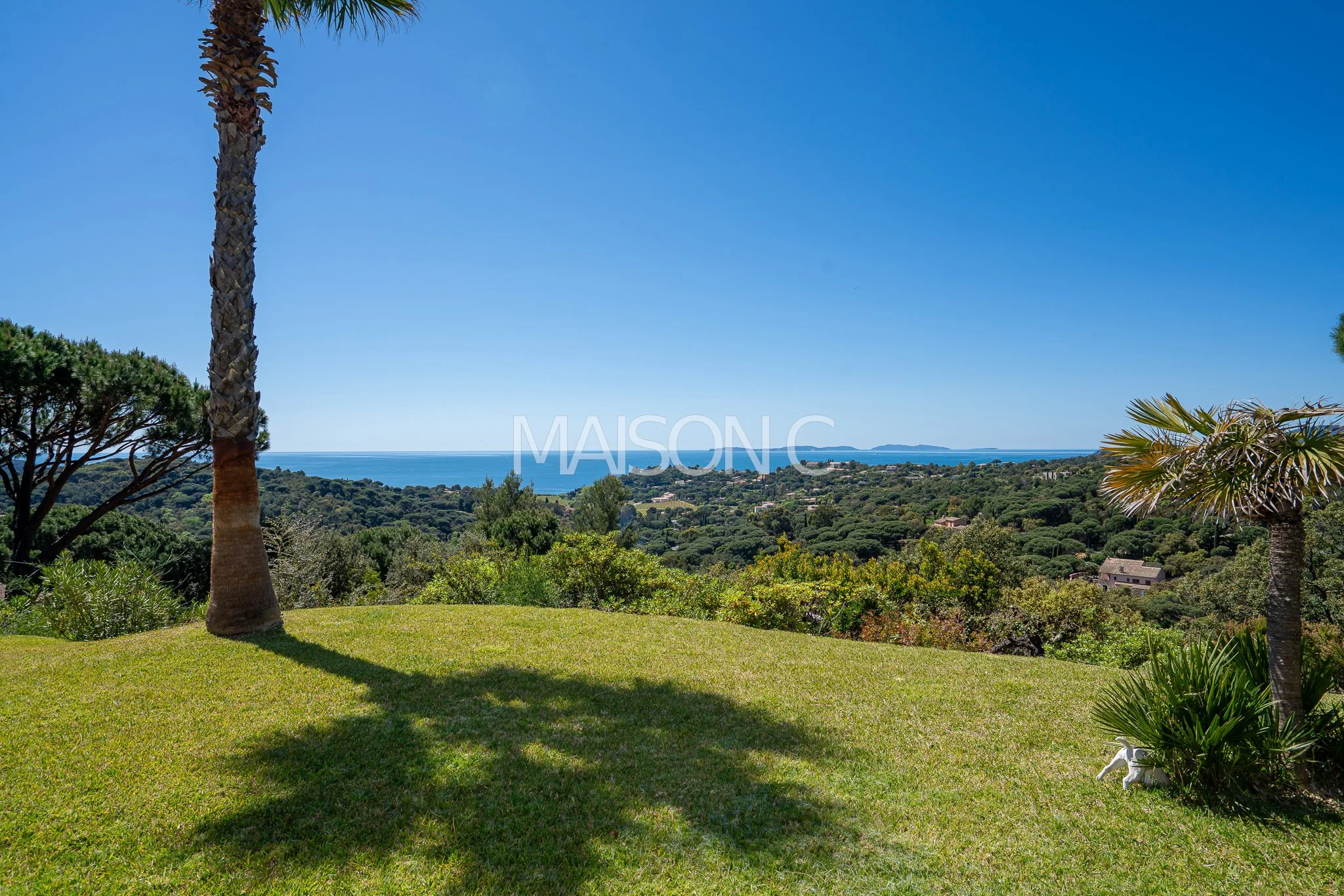 Paysage avec des palmiers, une pelouse verte, vue sur la mer et des îles à l'horizon en plein jour