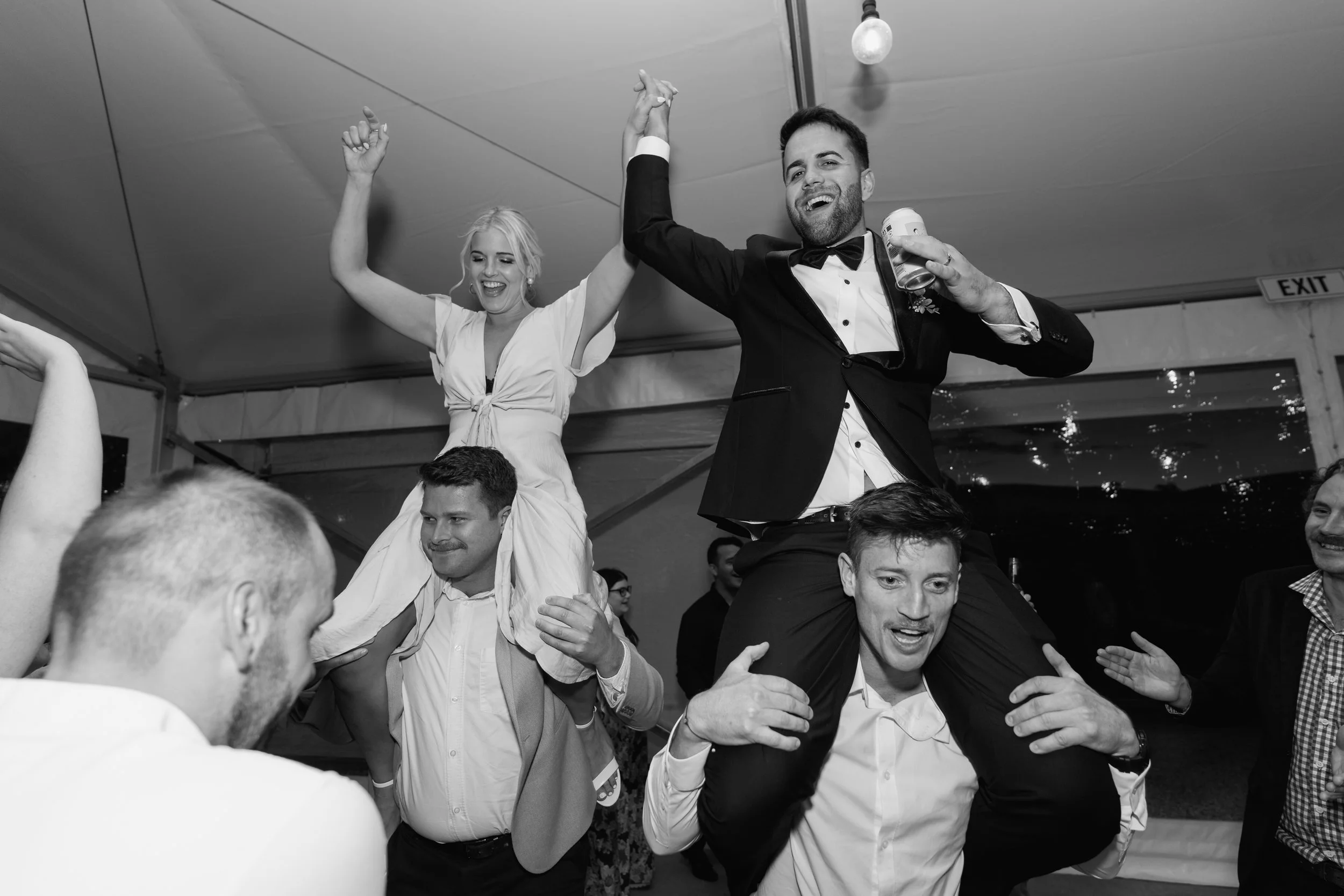 A group of people celebrating at a party, with a woman on someone's shoulders and a man holding her hand, smiling and raising their hands in celebration