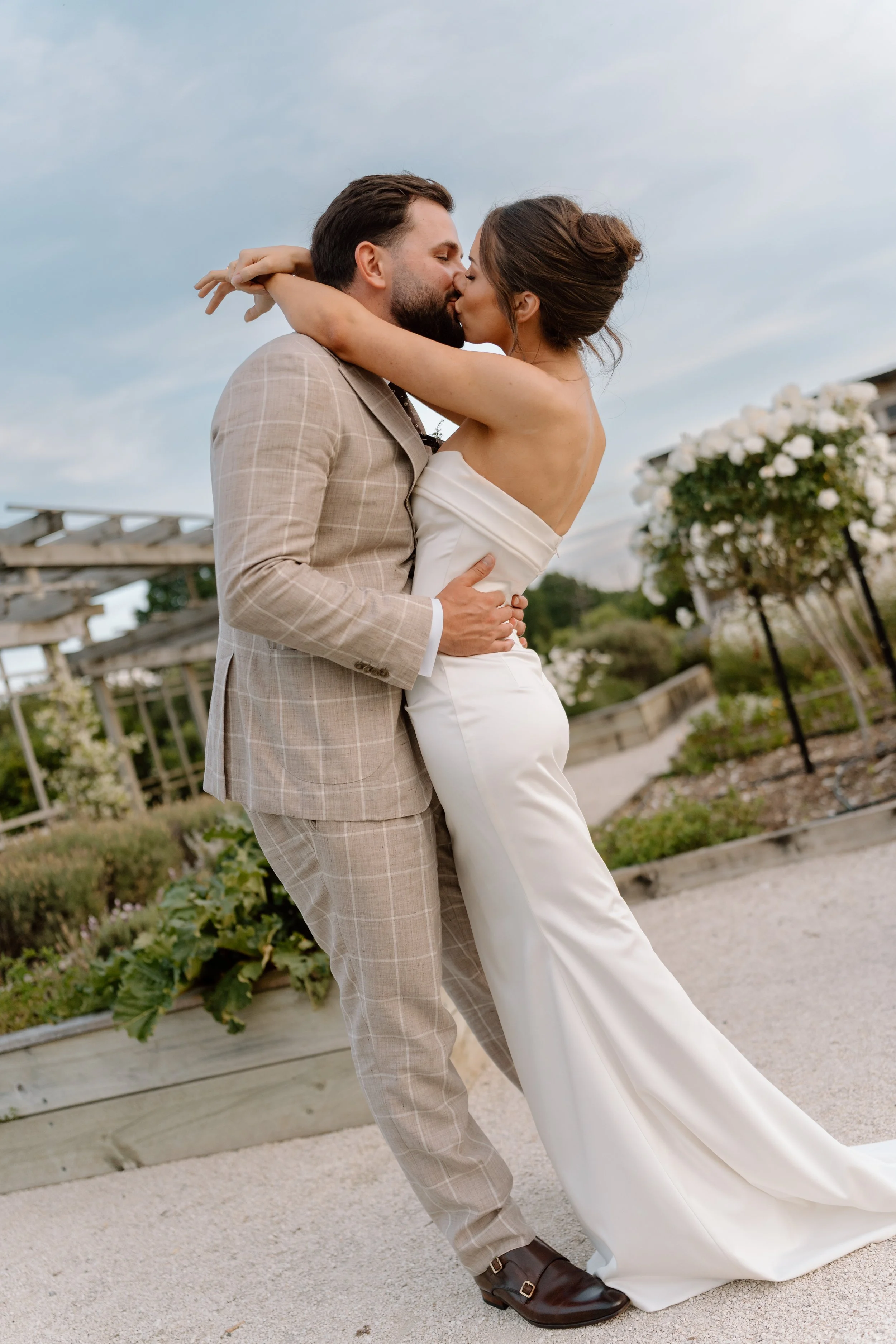 A couple in wedding attire sharing a kiss outdoors during daytime.