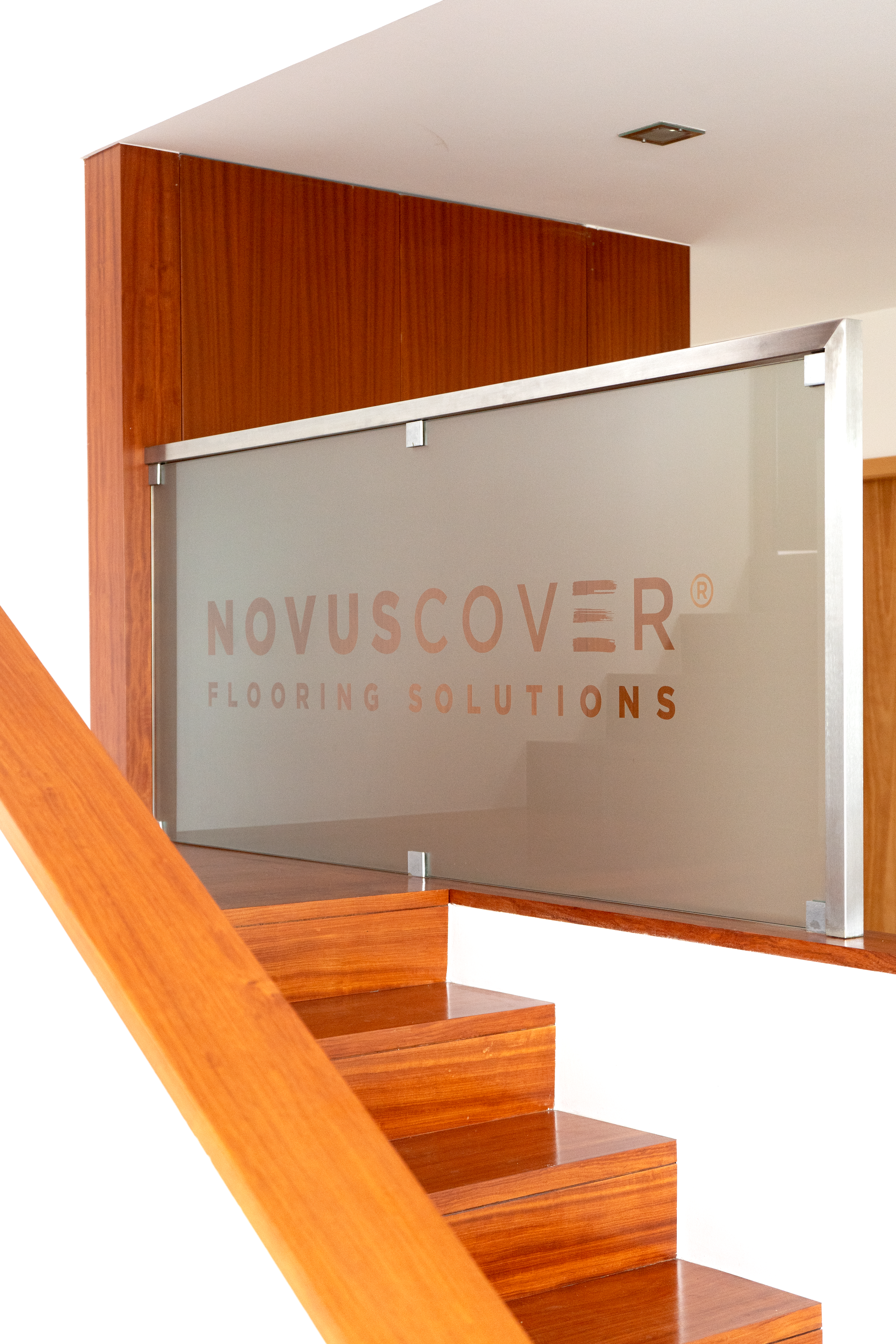 Escada de madeira com um vidro de proteção com o logo "Novuscover Flooring Solutions" ao fundo na parede.