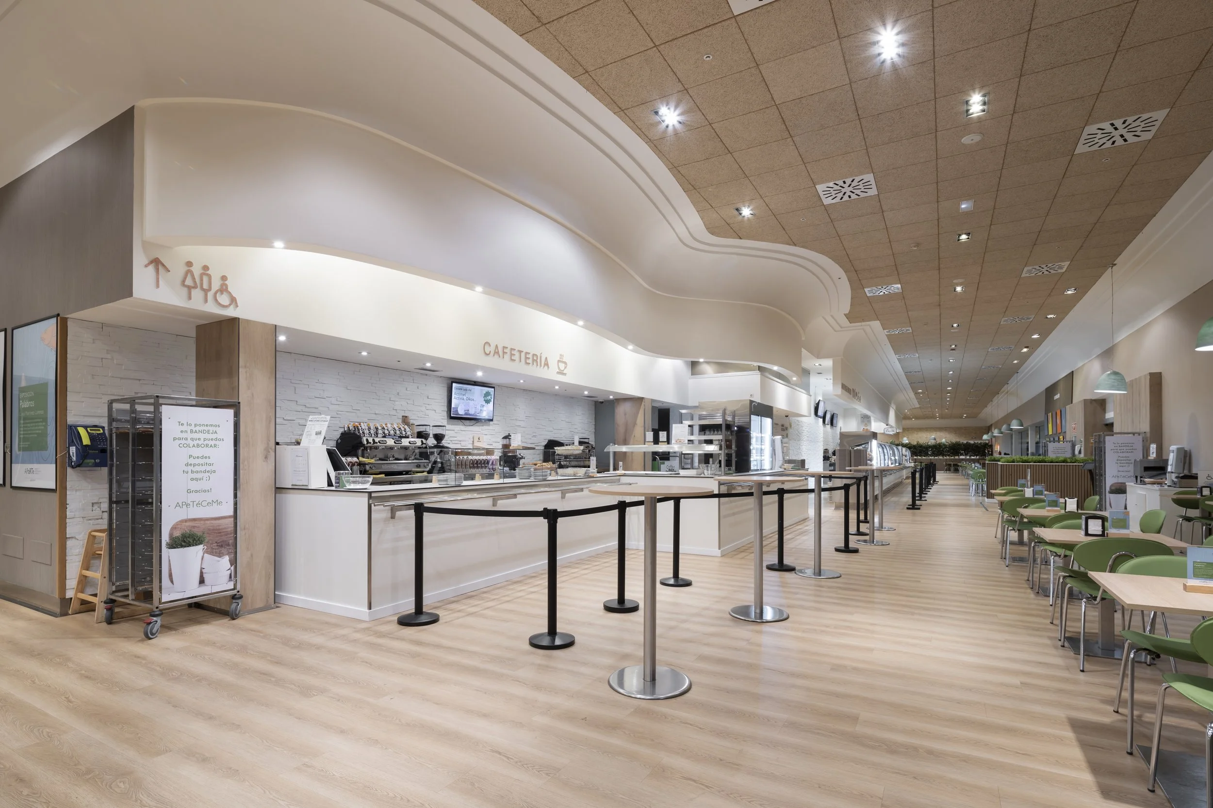 Interior de um café, com área de atendimento e mesas com cadeiras verdes.