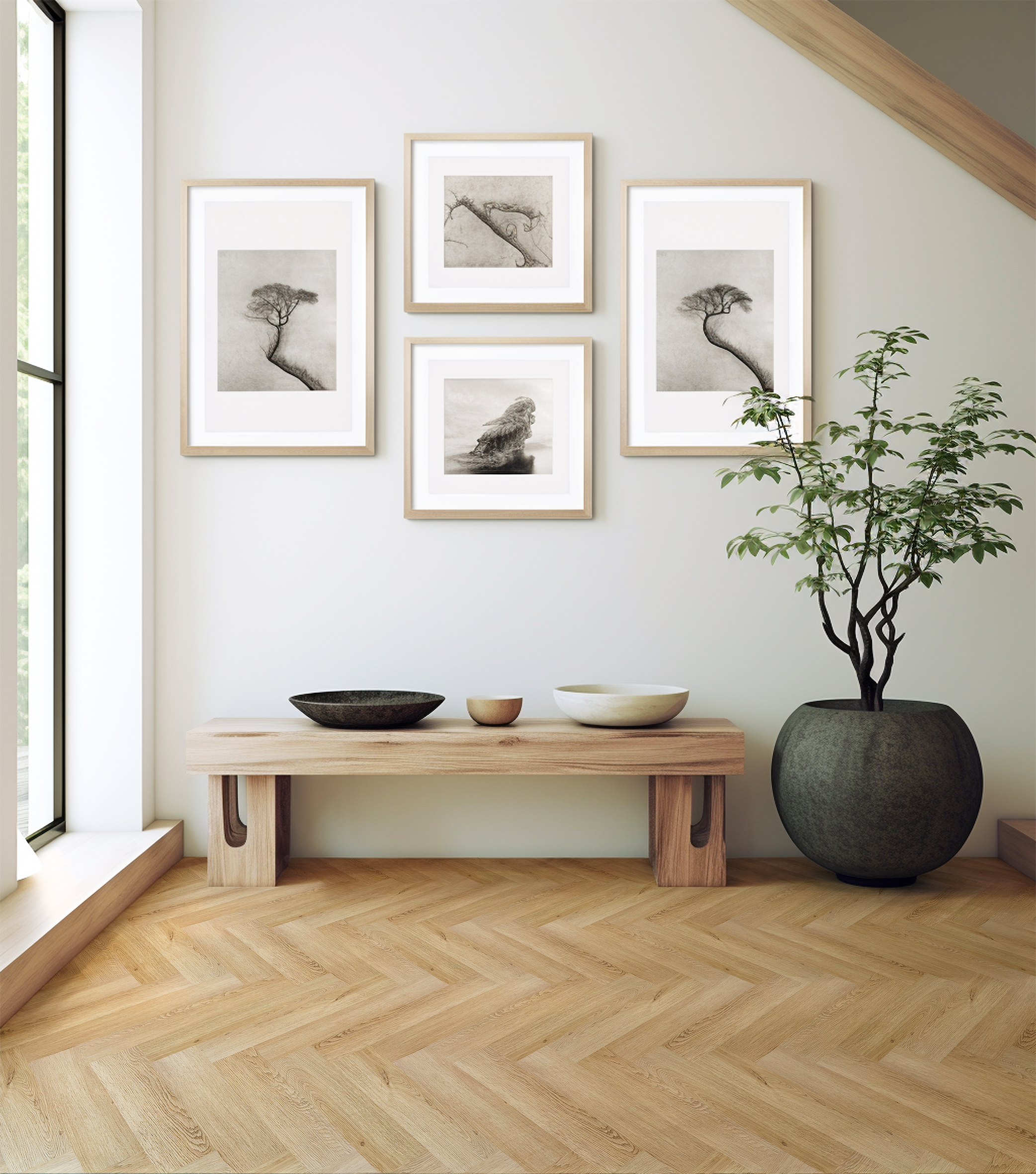 Quatro quadros com fotografias em preto e branco de árvores e uma formação rochosa, decoram uma parede branca. Há uma planta em um vaso grande ao lado de uma mesa de apoio de madeira, com três pratos decorativos.