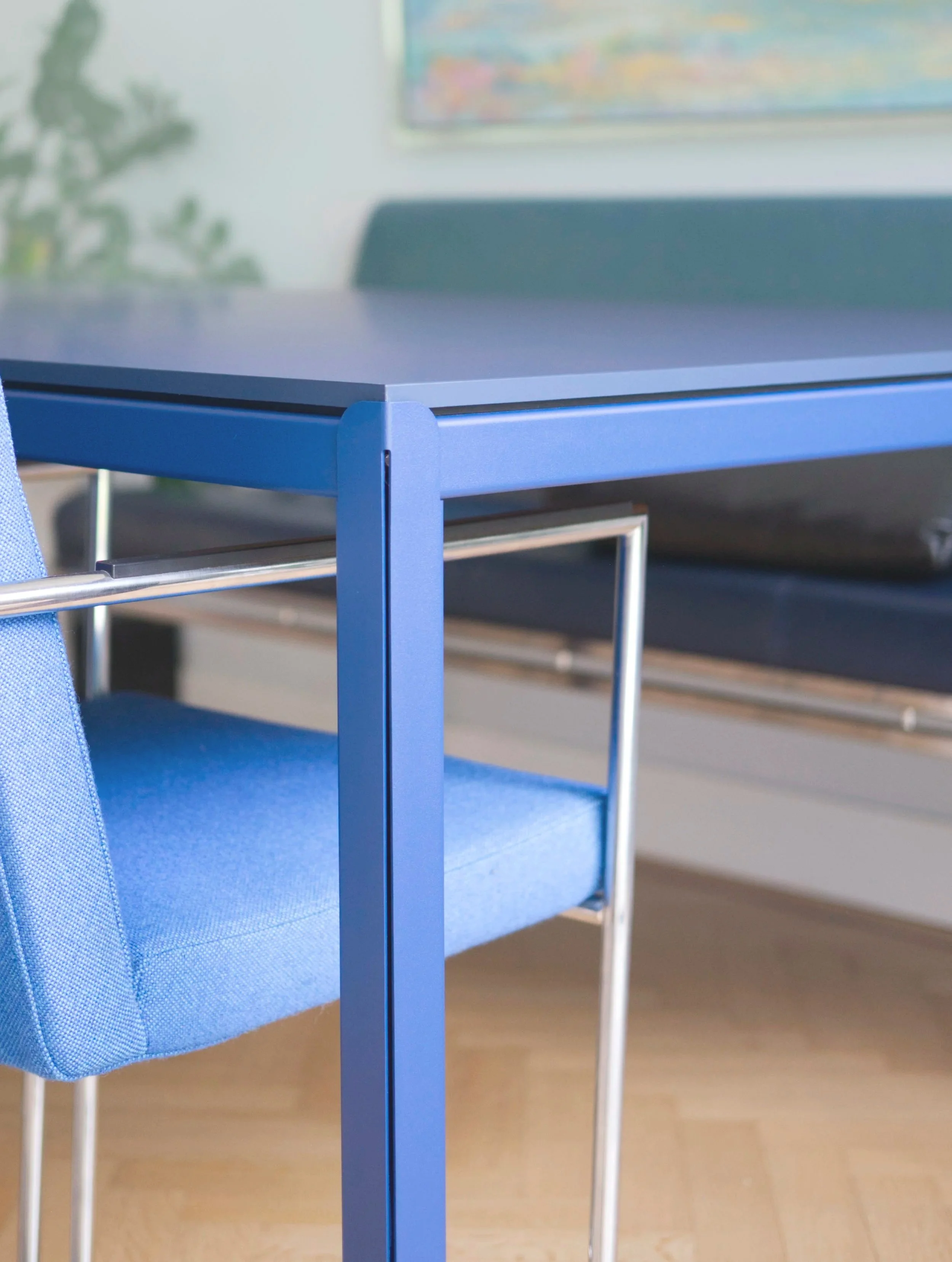 Close-up van een blauwe tafel en een blauw beklede stoel in een kantoor of woonruimte.