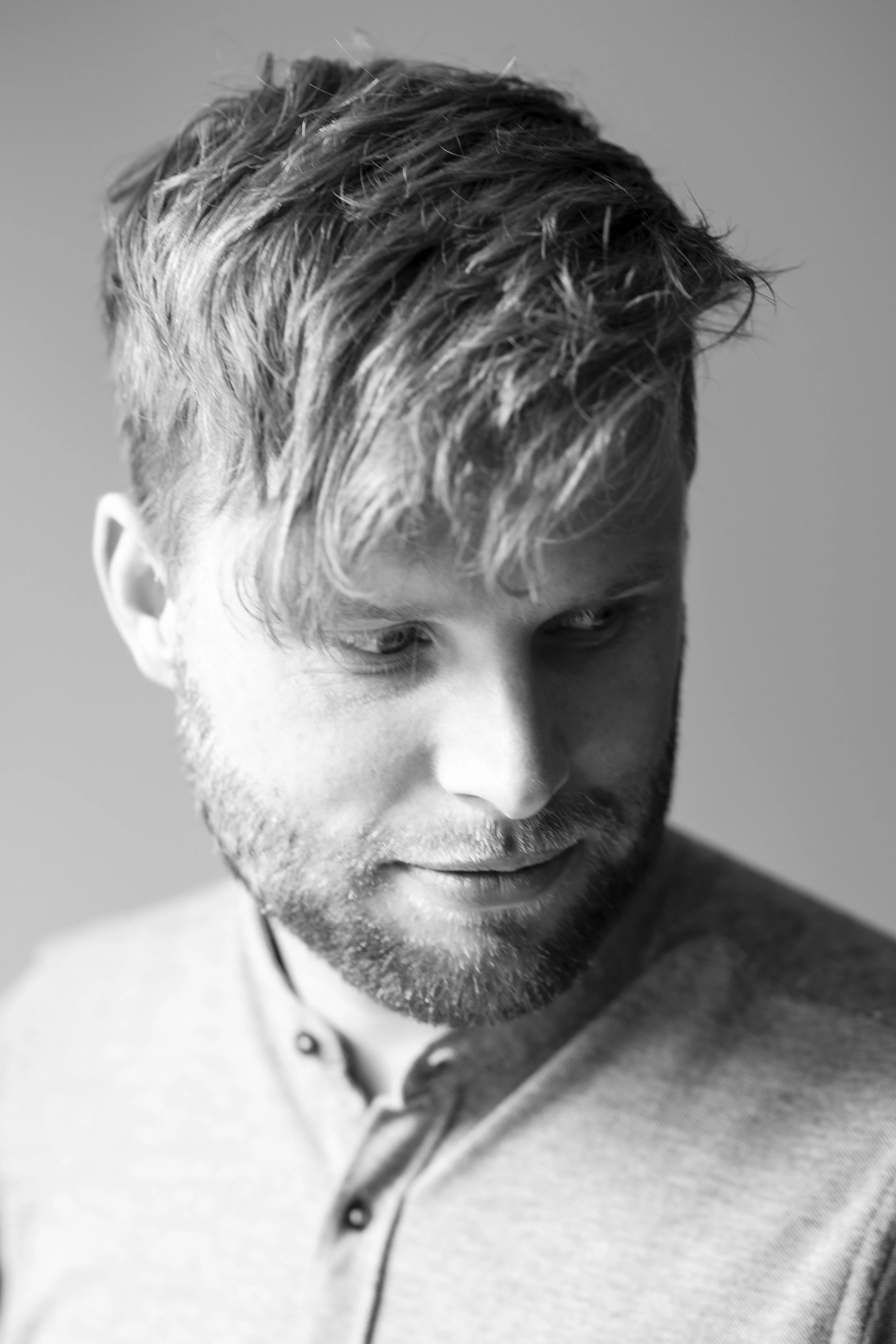 Zwart-witfoto van een man met een baard en warrig haar, die naar beneden kijkt.