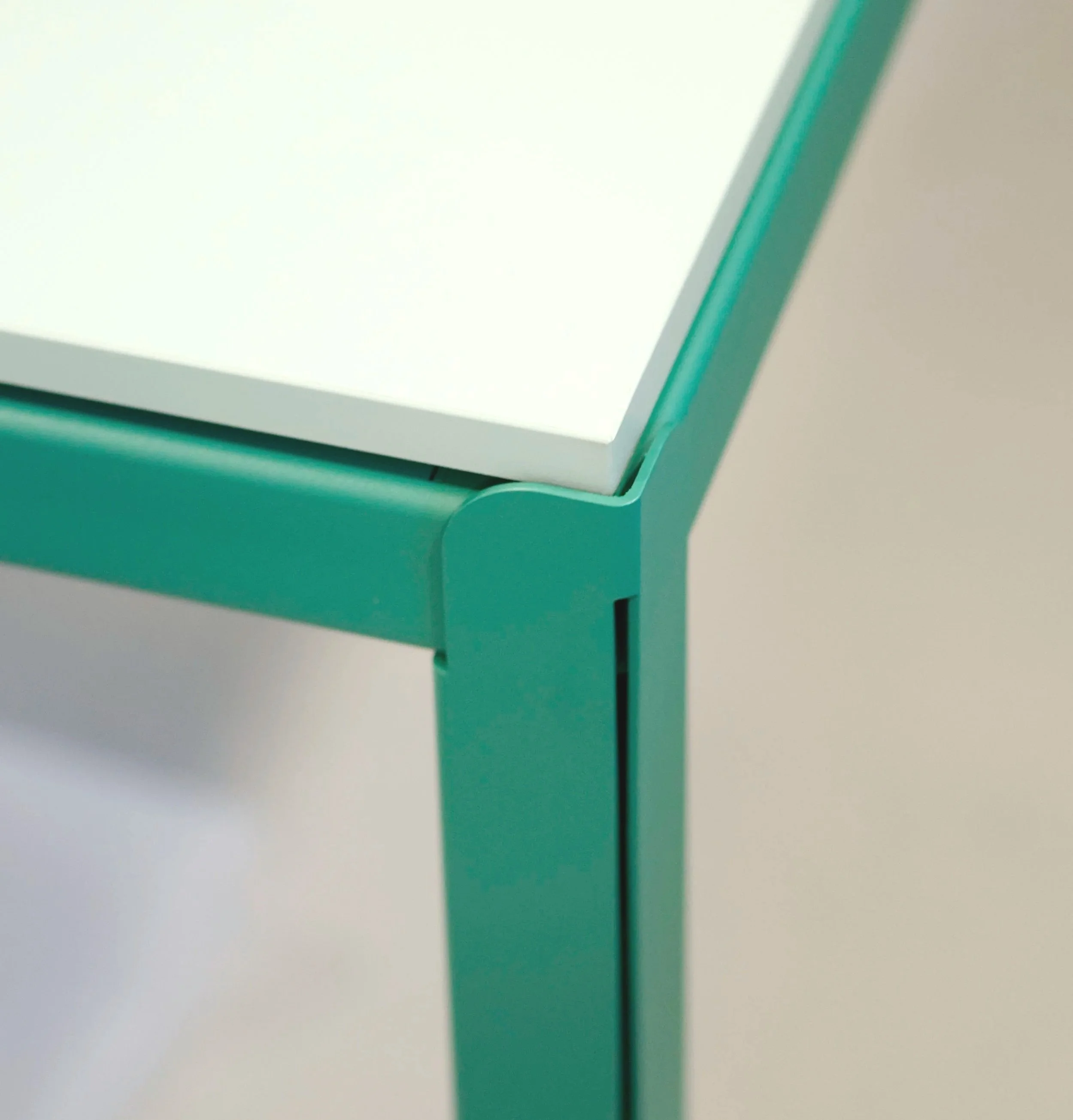 Een close-up van de hoek van een tafel met een groene metalen frame en een wit tafelblad.
