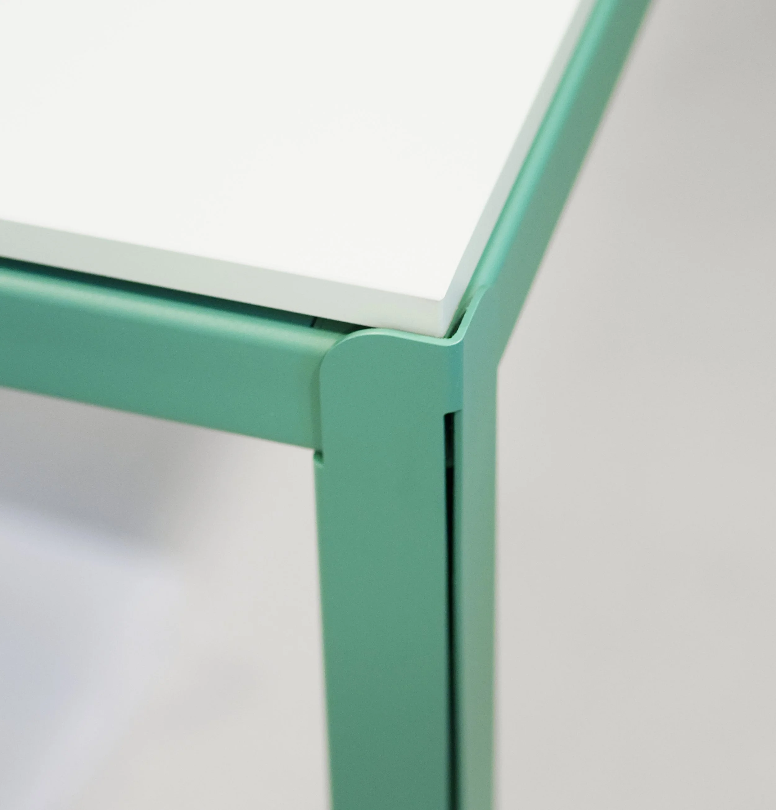 Close-up van een groene metalen tafel met een witte bovenkant, onderdeel van het tafelblad en de poten zichtbaar.
