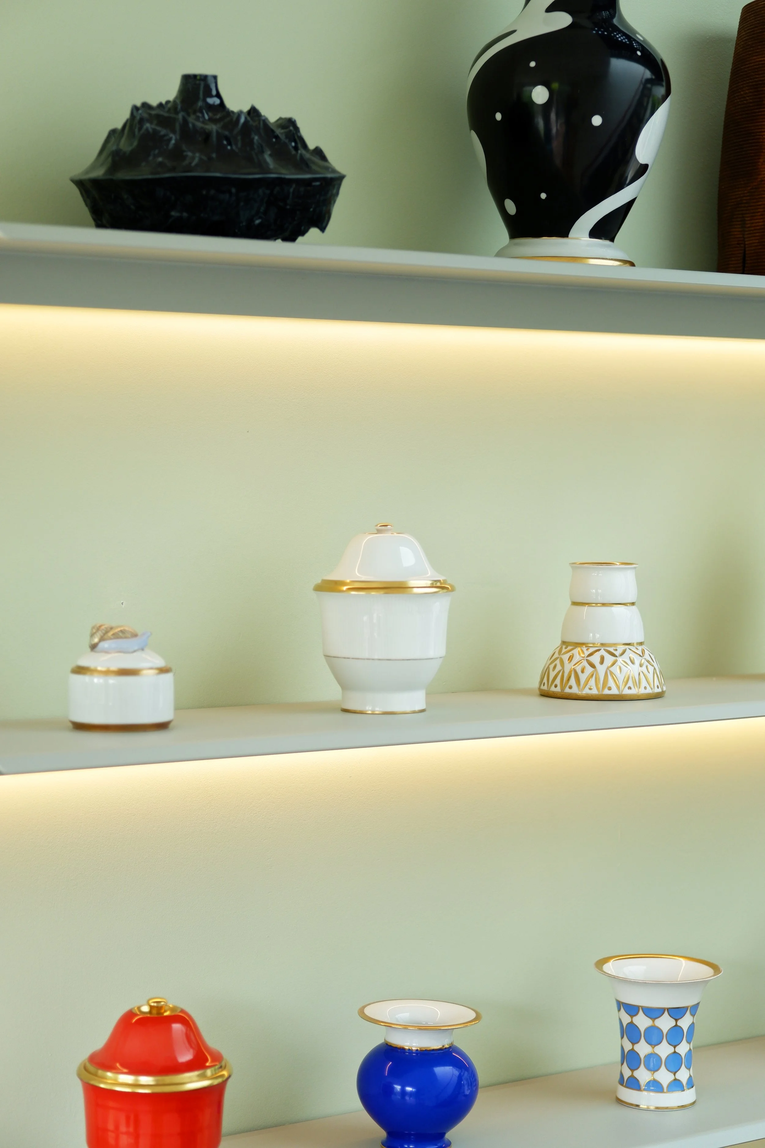 Decoratieve vazen en kommen op een lichtgroene planken en planken met ingebouwd verlichtingskanaal.