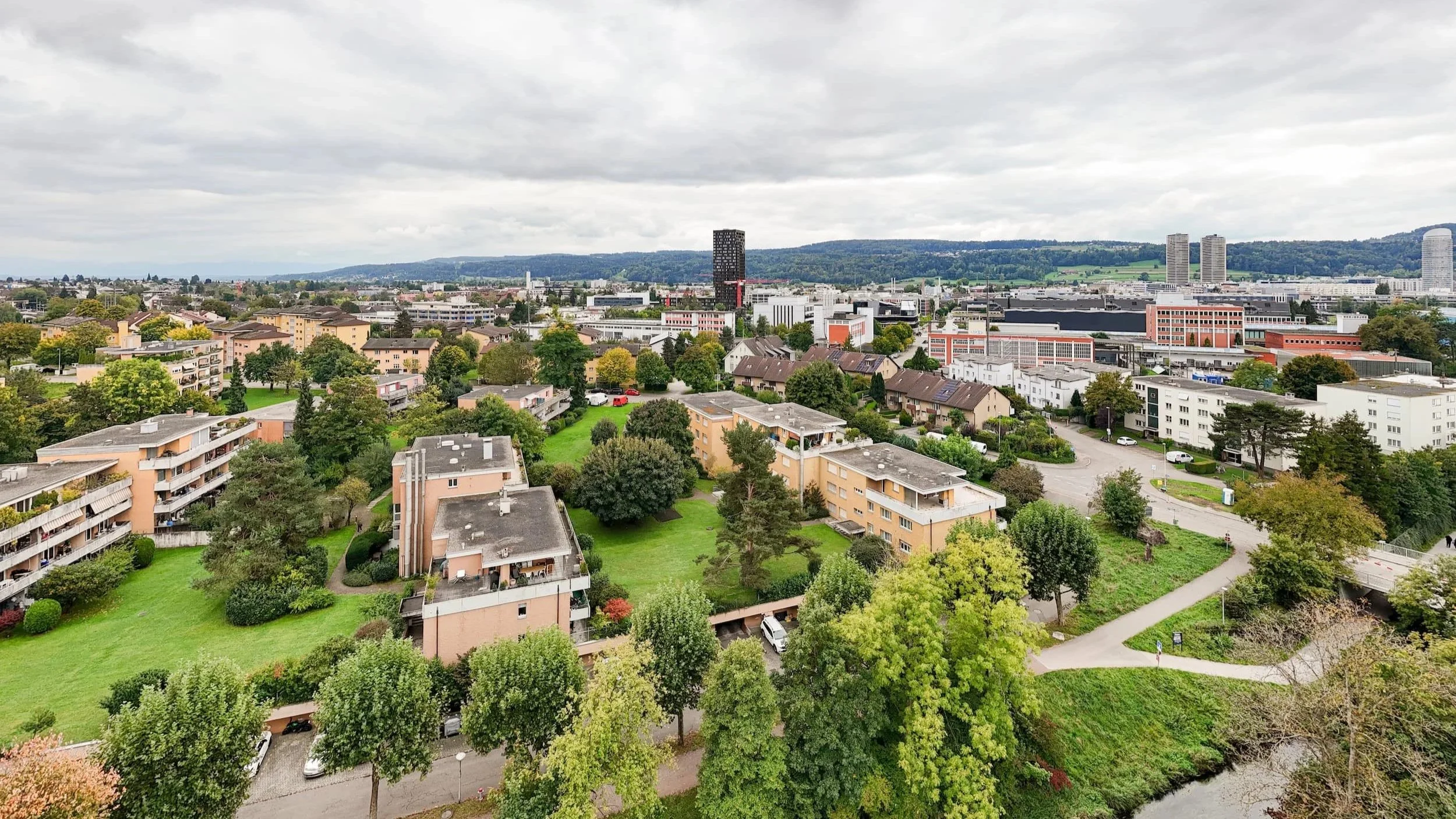 Stadtaufnahme mit Wohngebäuden, parks, Straßen, Fluss und skyline bei bewölktem Himmel.