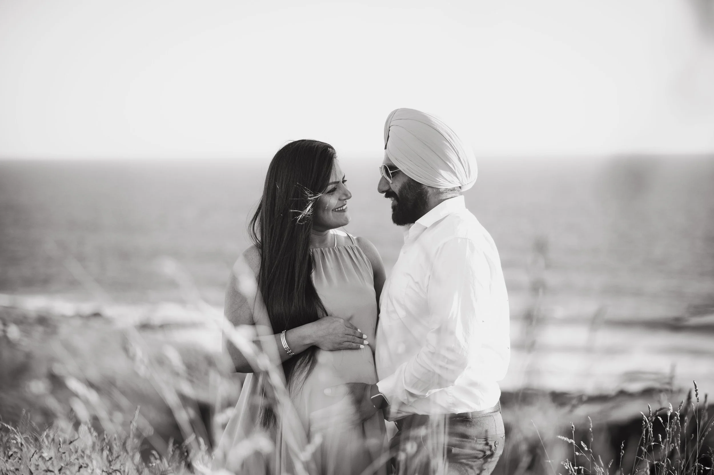 A couple standing close by the sea, smiling and looking into each other's eyes