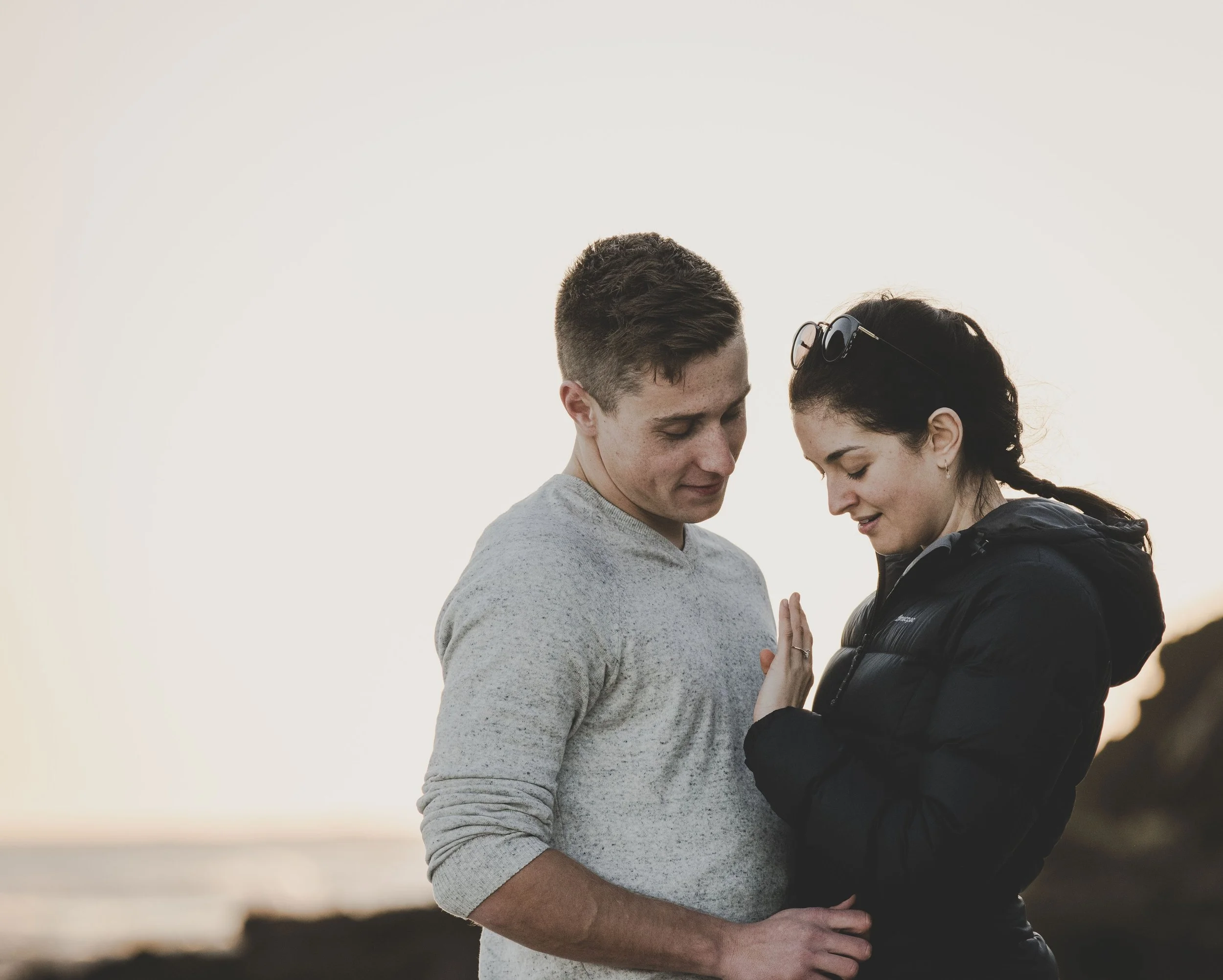 A young couple on a beach at sunset, looking at each other tenderly with their foreheads almost touching.