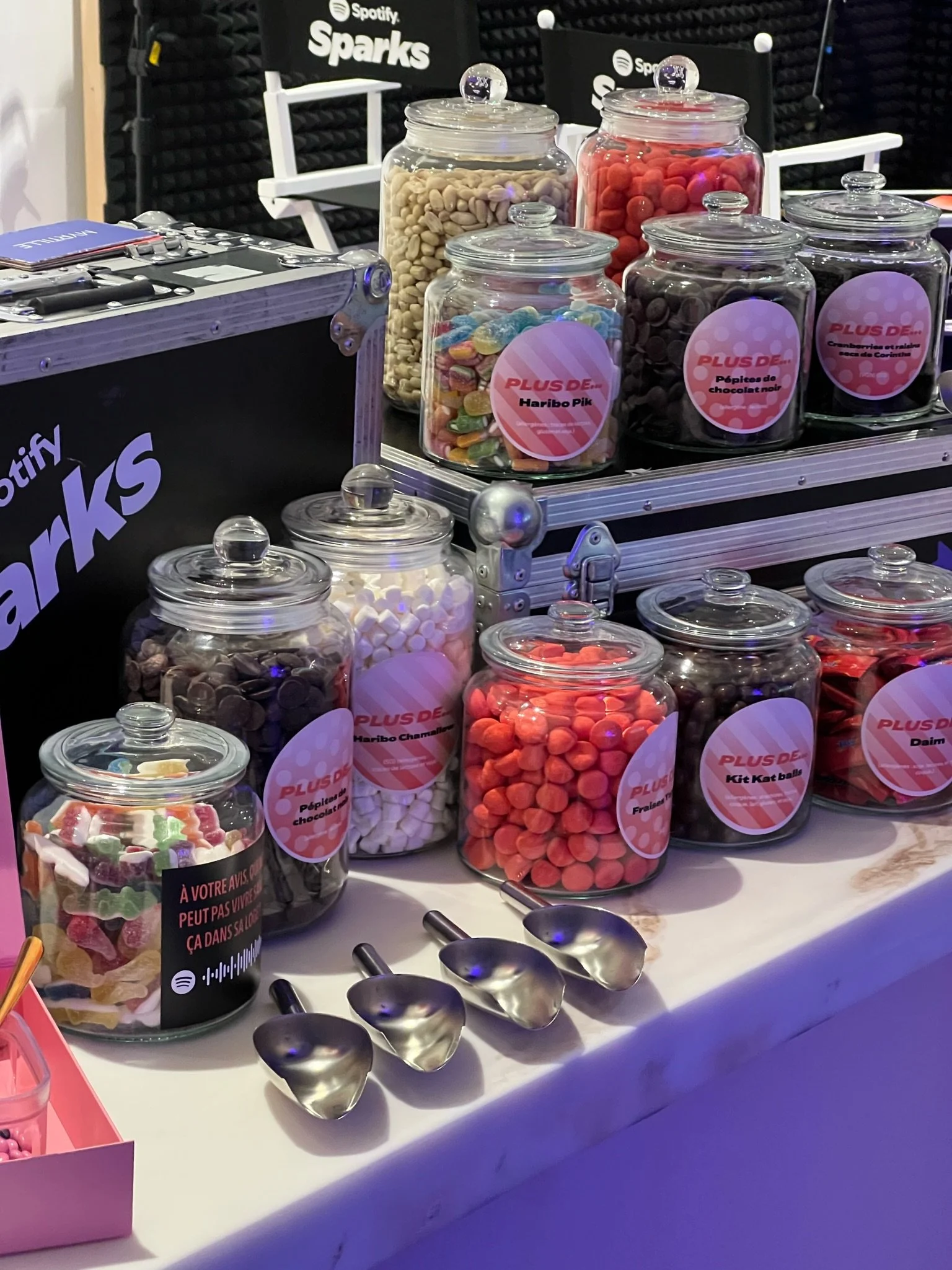 Various jars of colorful candies on a table with metal scoops, at a Spotify Sparks event.