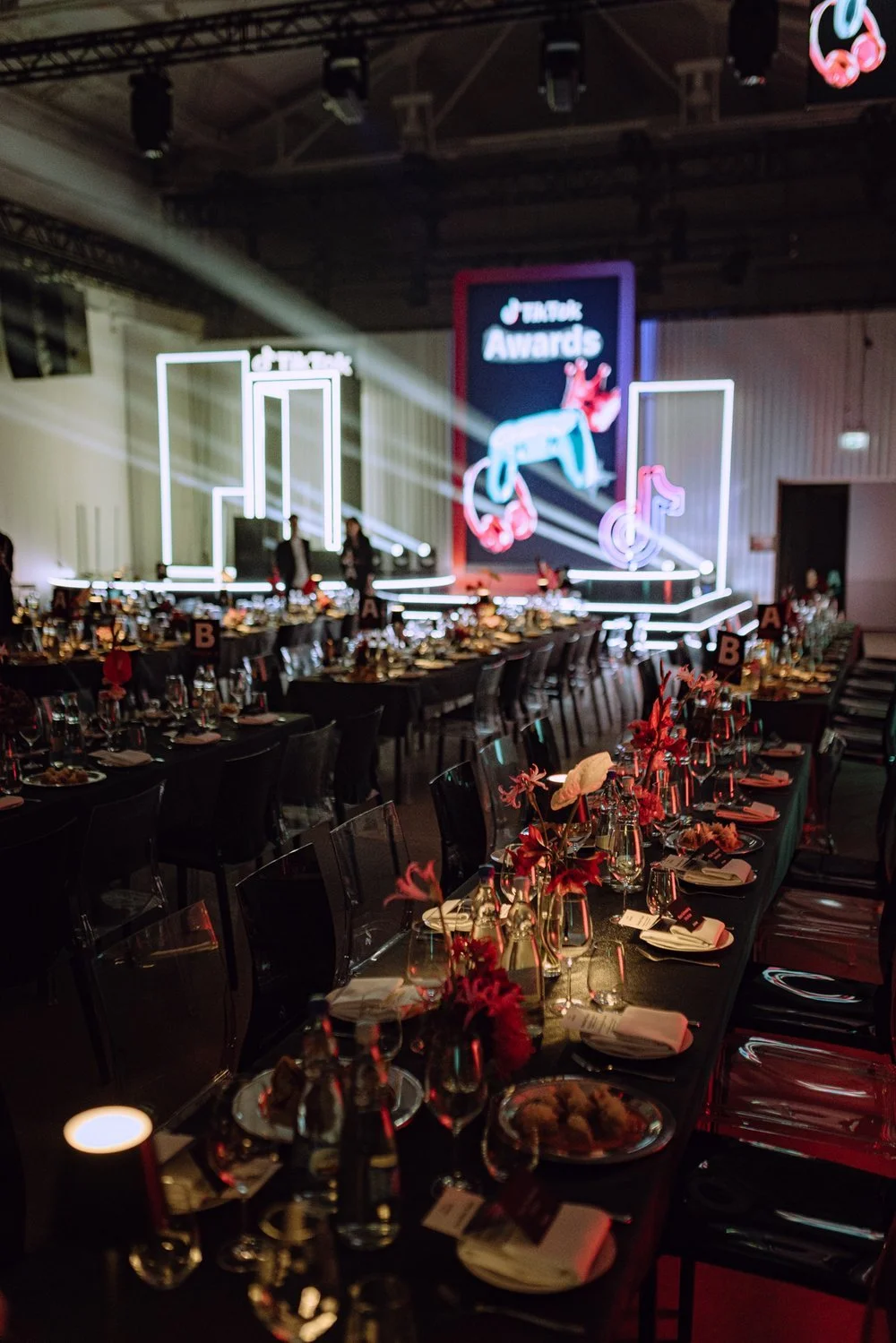 Empty decorated banquet hall with arranged tables and a stage with neon lights and a large screen displaying TikTok Awards logo.