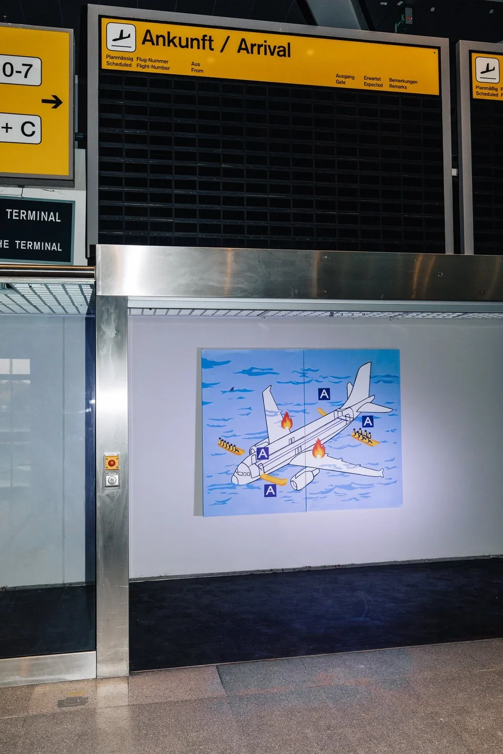 Signboard showing airplane arrival information and a safety poster depicting an emergency evacuation plan on an airplane.