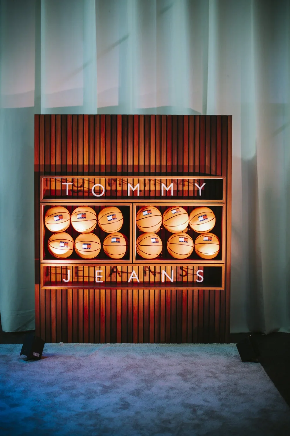 Display of basketballs arranged in a wooden cabinet with a sign reading 'TOMMY JEANS'.