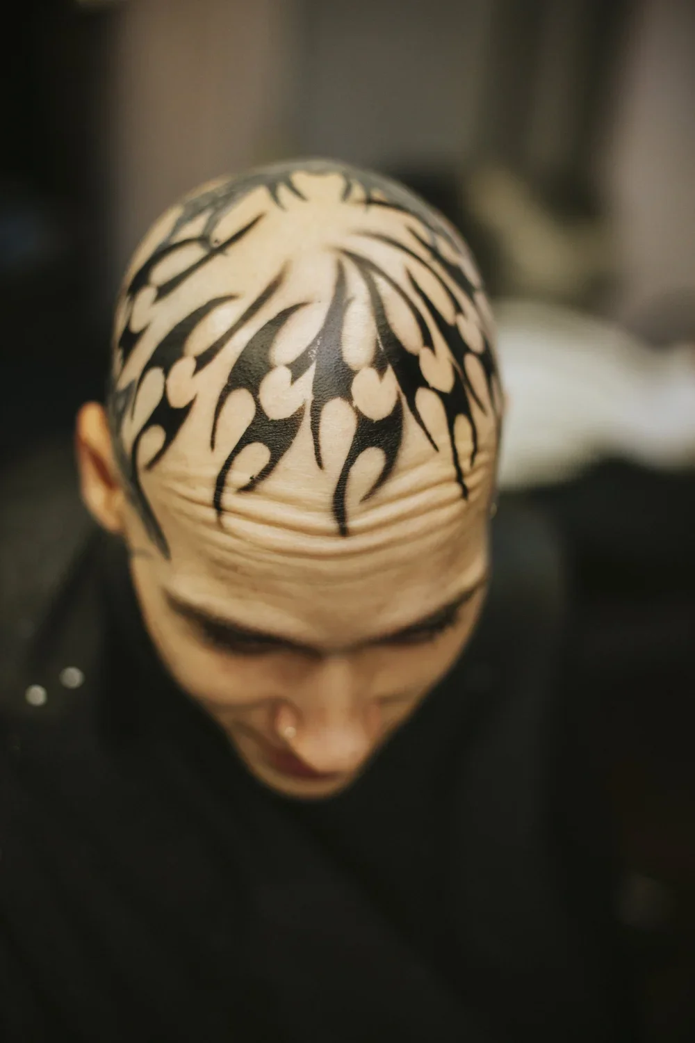 A person with black and white tribal-style face paint or tattoo designs on their bald head, looking downward.