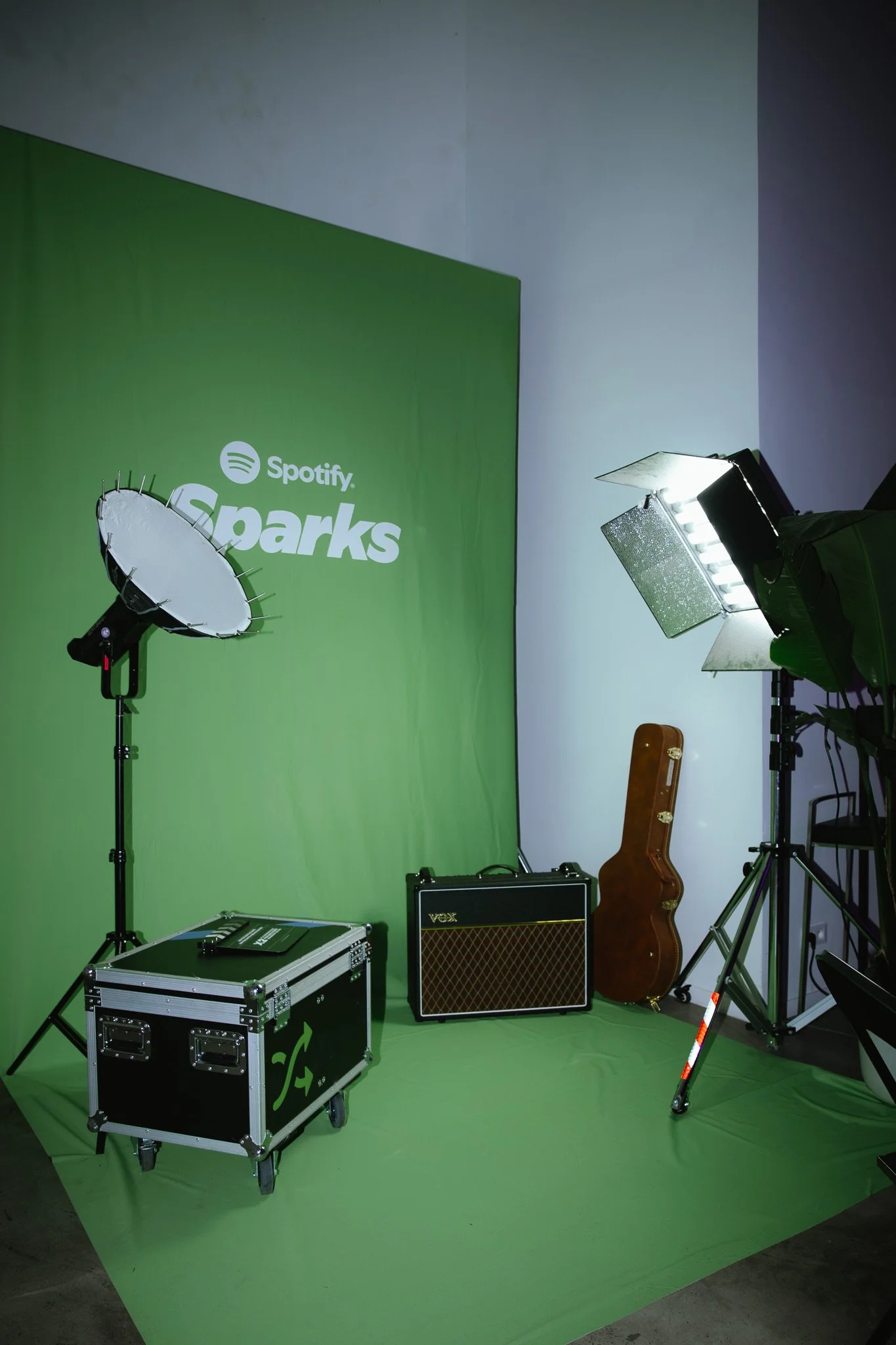 Green screen setup with professional lighting, musical instrument case, guitar amplifier, and a stool, with a Spotify Sparks logo on the backdrop.