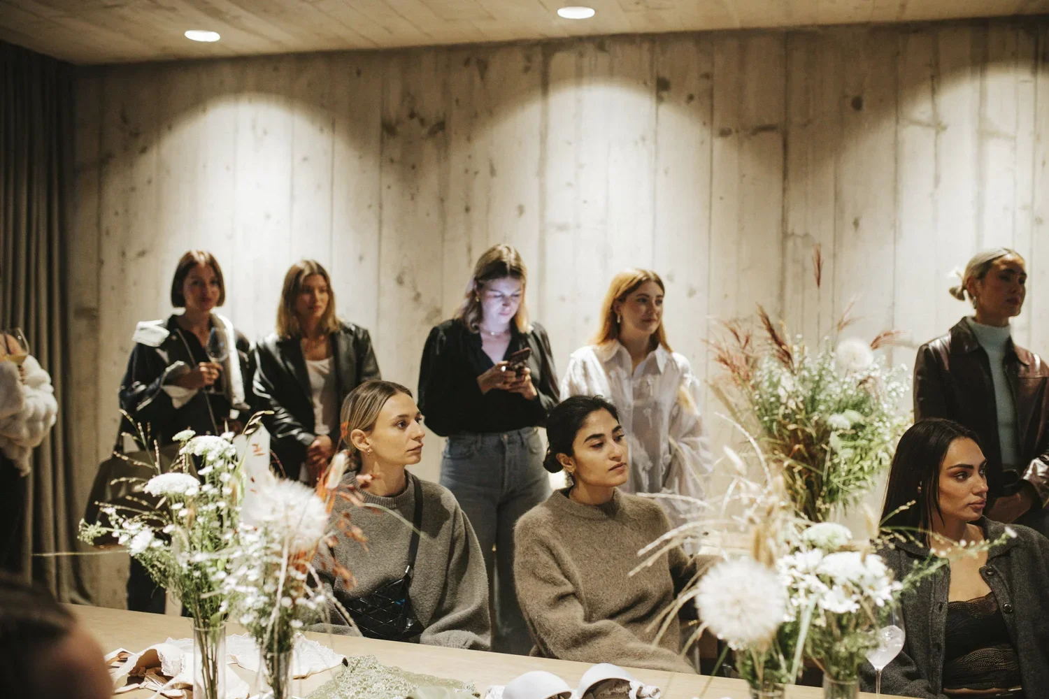 Group of women in a room with floral decorations, some seated and some standing, appearing to attend an event or gathering.