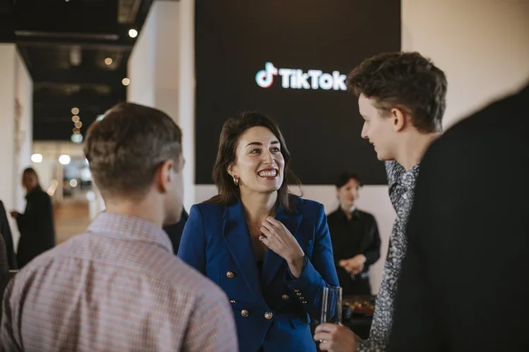 People talking at a professional event with a TikTok logo in the background.