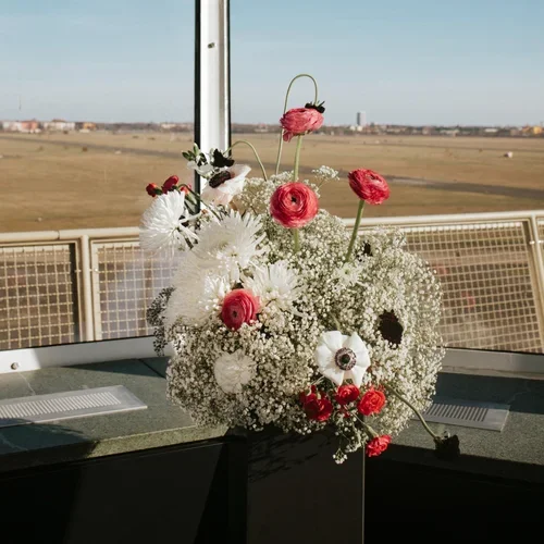 Flower arrangement with white and red flowers on a window sill overlooking a flat landscape.