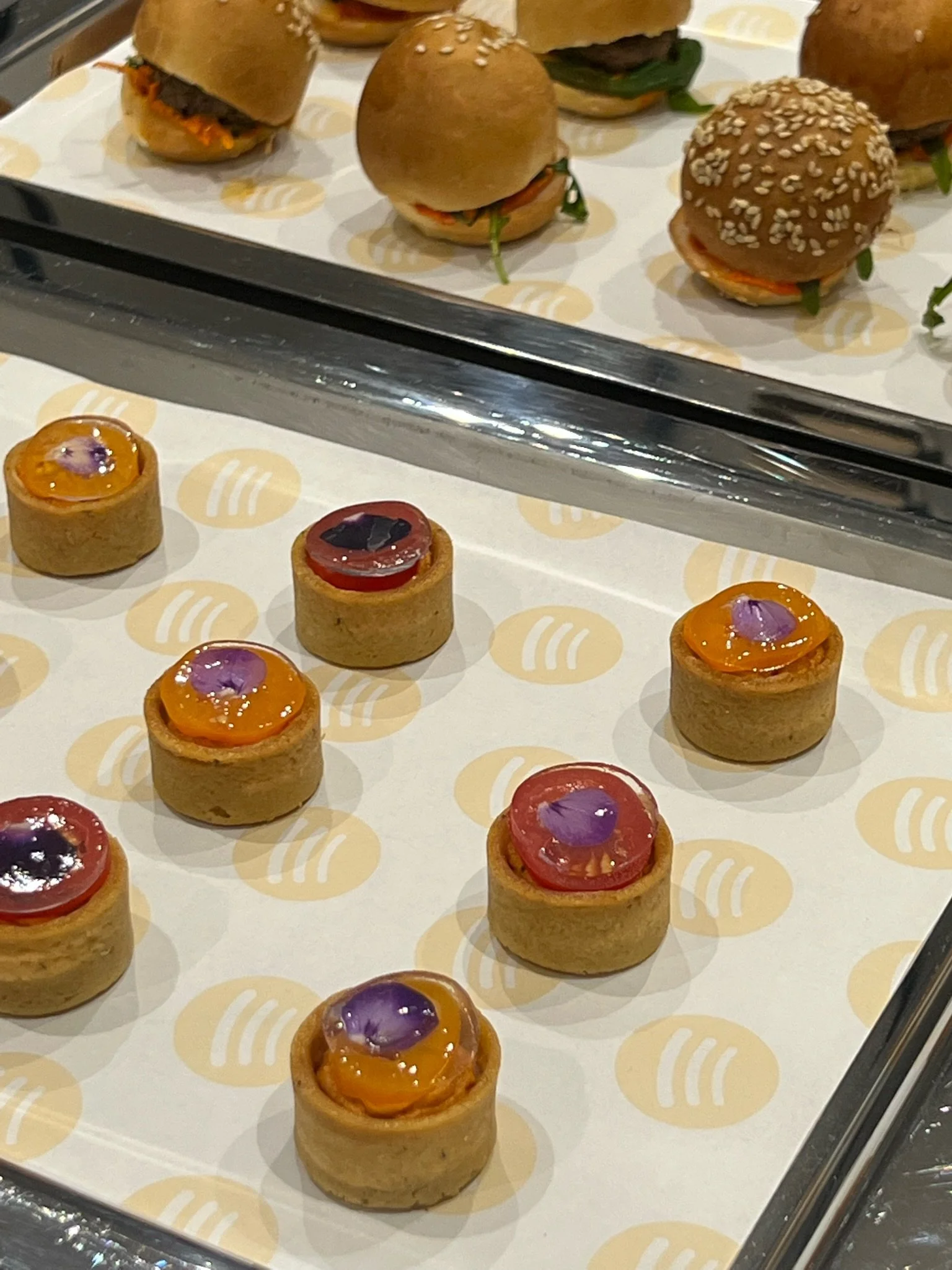 Mini tartlets with colorful jam and purple edible flowers, arranged on a tray.