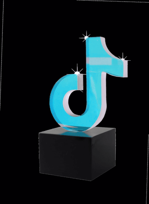 A shiny, light blue TikTok logo sculpture with reflective sparkles, mounted on a black pedestal, against a dark background.