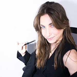 Young woman with brown hair holding a pen, leading a meeting or presentation in an office setting.