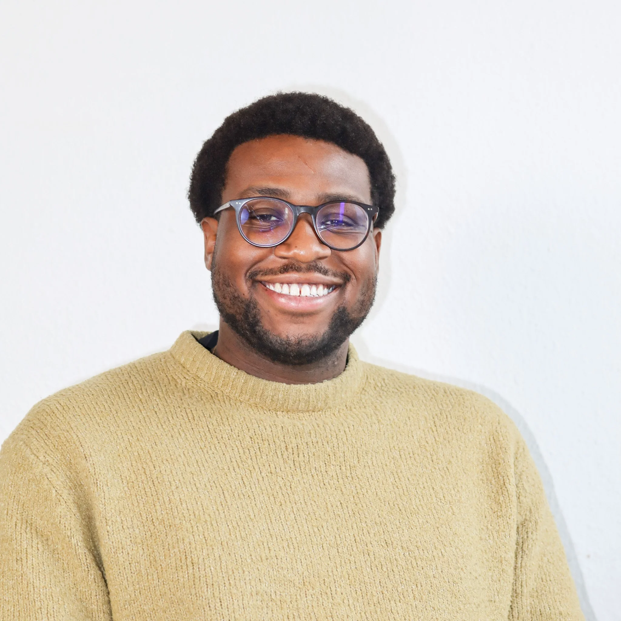 Portrait of a man wearing glasses and a green sweater, looking slightly to the side against a white background.