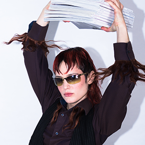 Woman with red hair and sunglasses lifting a large stack of papers or files over her head