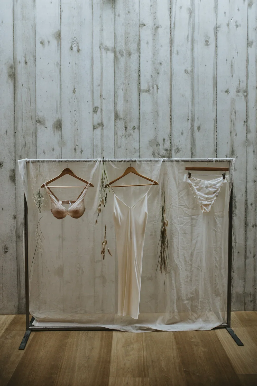 Clothing and lingerie hanging on a garment rack against a rustic, whitewashed wooden wall.