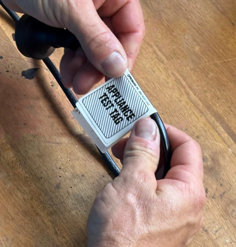 electrician holding an electrical cord placing a tagging compliance sticker in a business in Perth