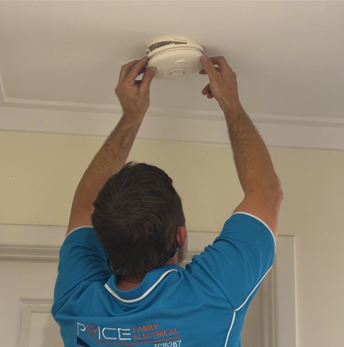 Image of a residential electrician installing a smoke detector in a home in Perth