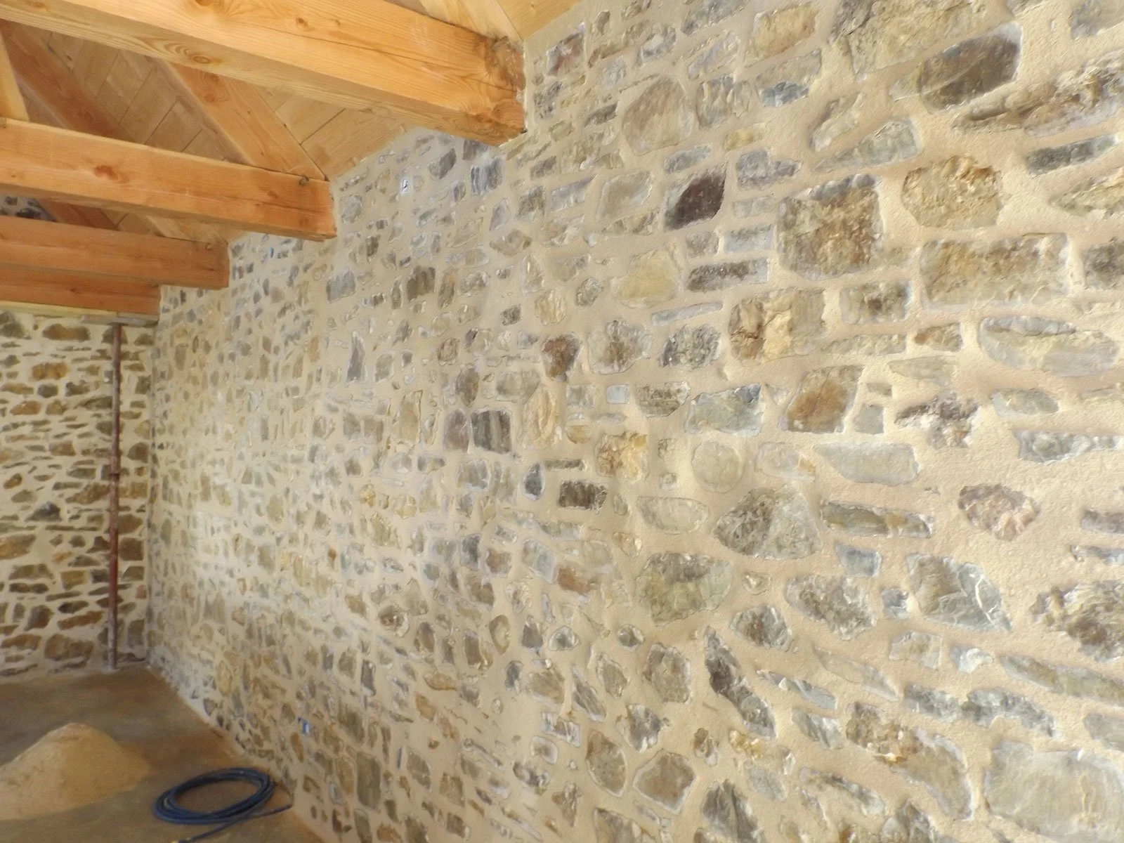 Mur en pierre avec des poutres en bois au plafond dans une pièce intérieure.