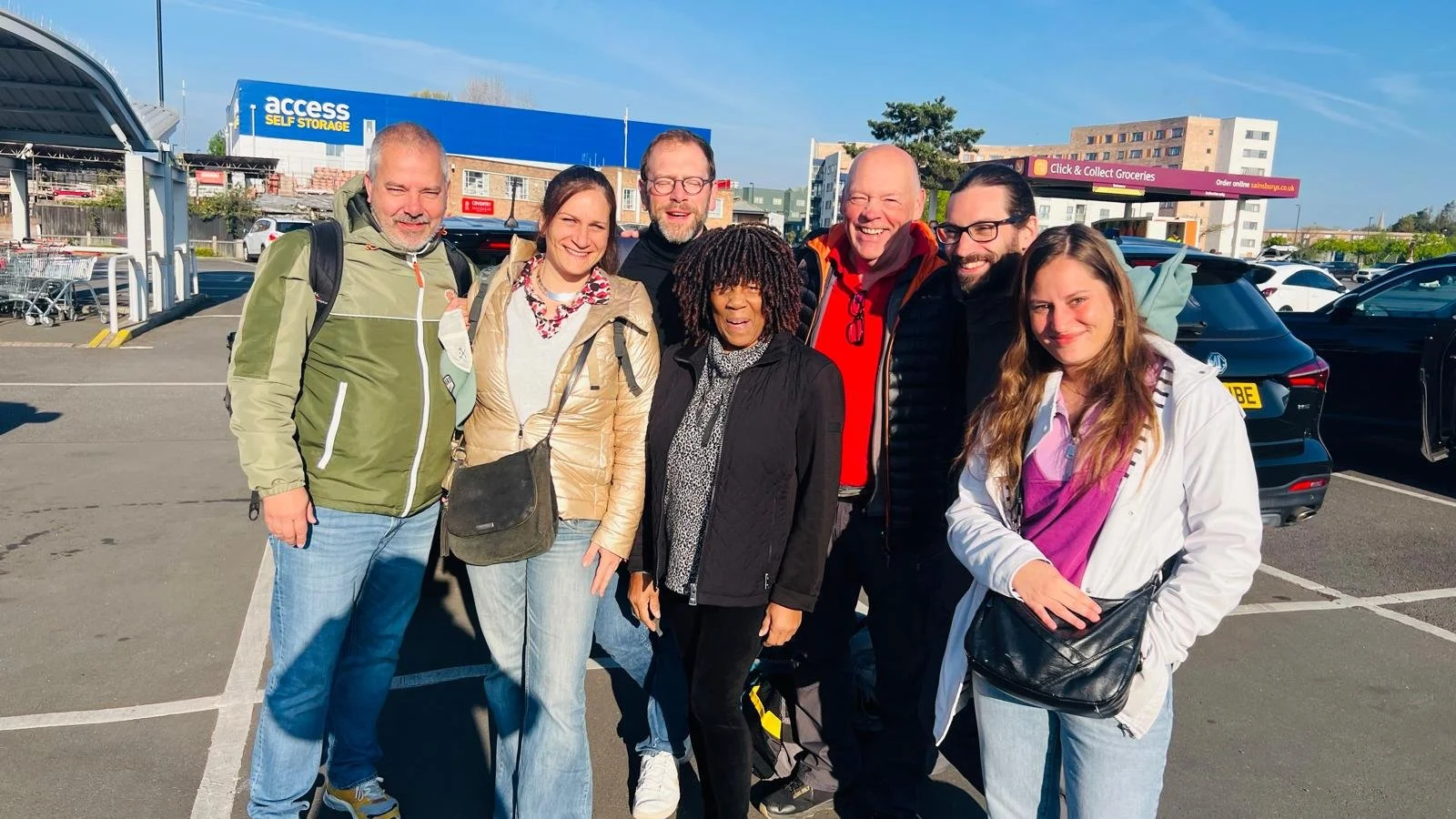 Scenic view of a lake surrounded by rolling green hills and mountain ranges in the distance with overcast sky.