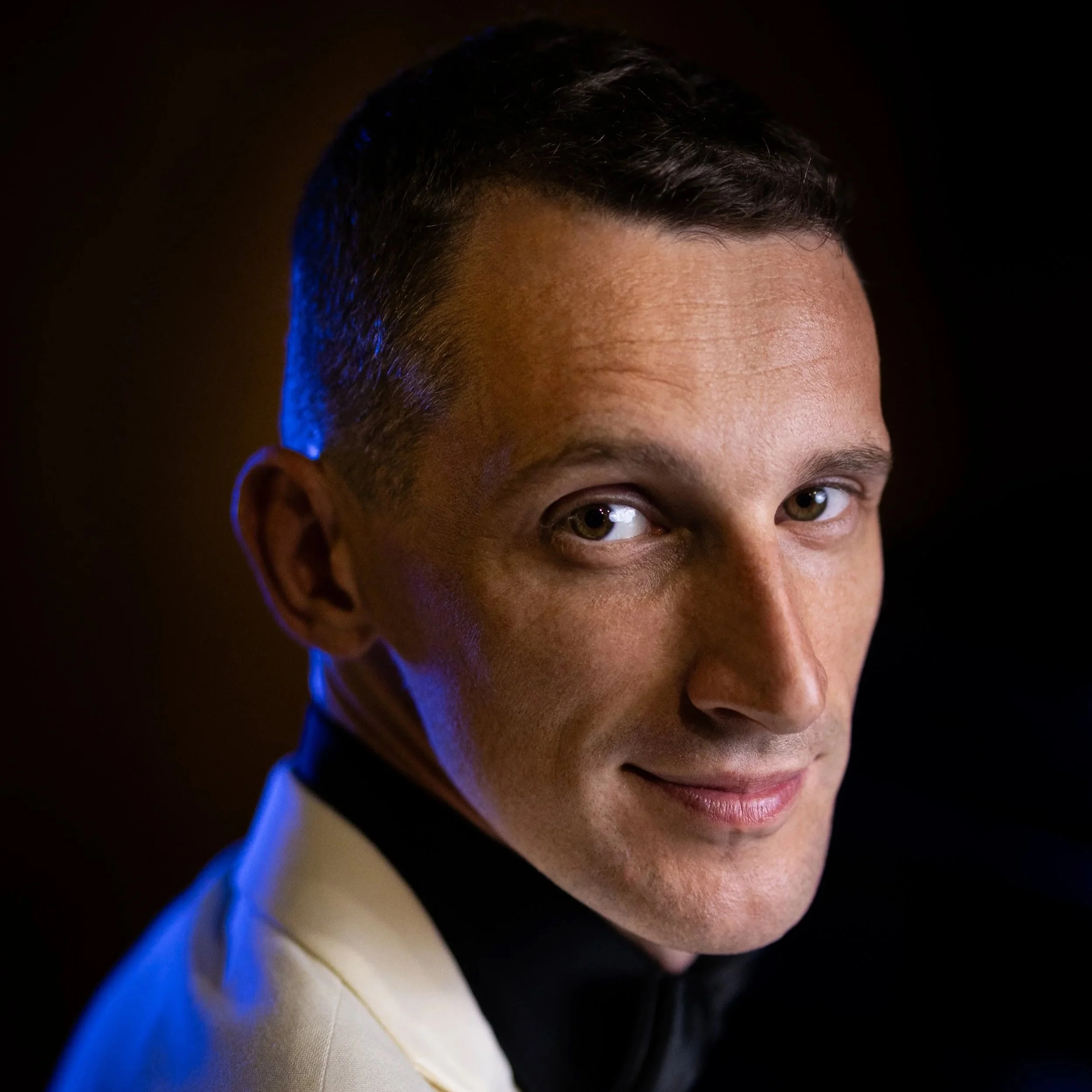 Professional cinematic portrait photography with dramatic blue rim light and warm tones, male subject in white blazer