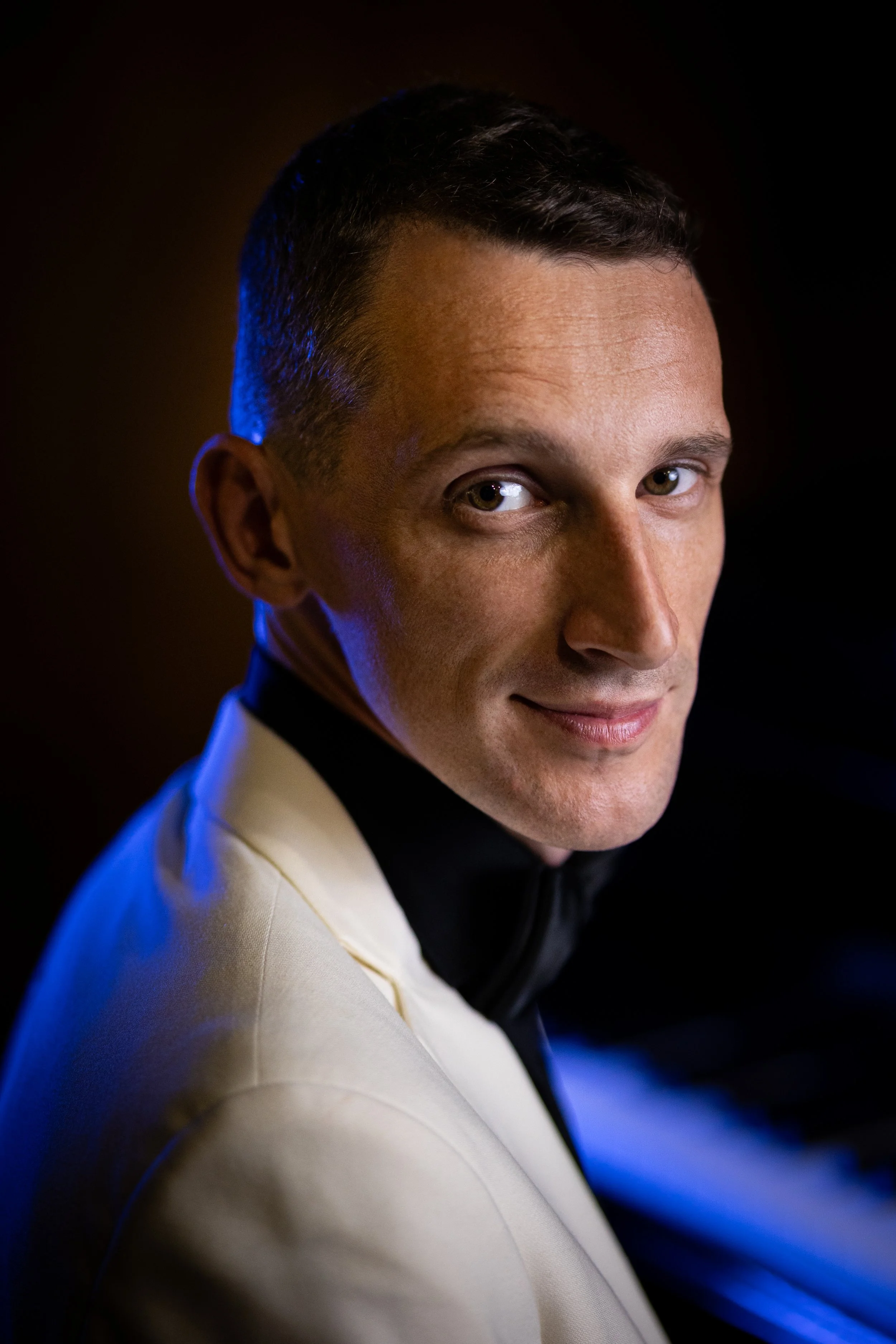 Professional cinematic portrait photography with dramatic blue rim light and warm tones, male subject in white blazer