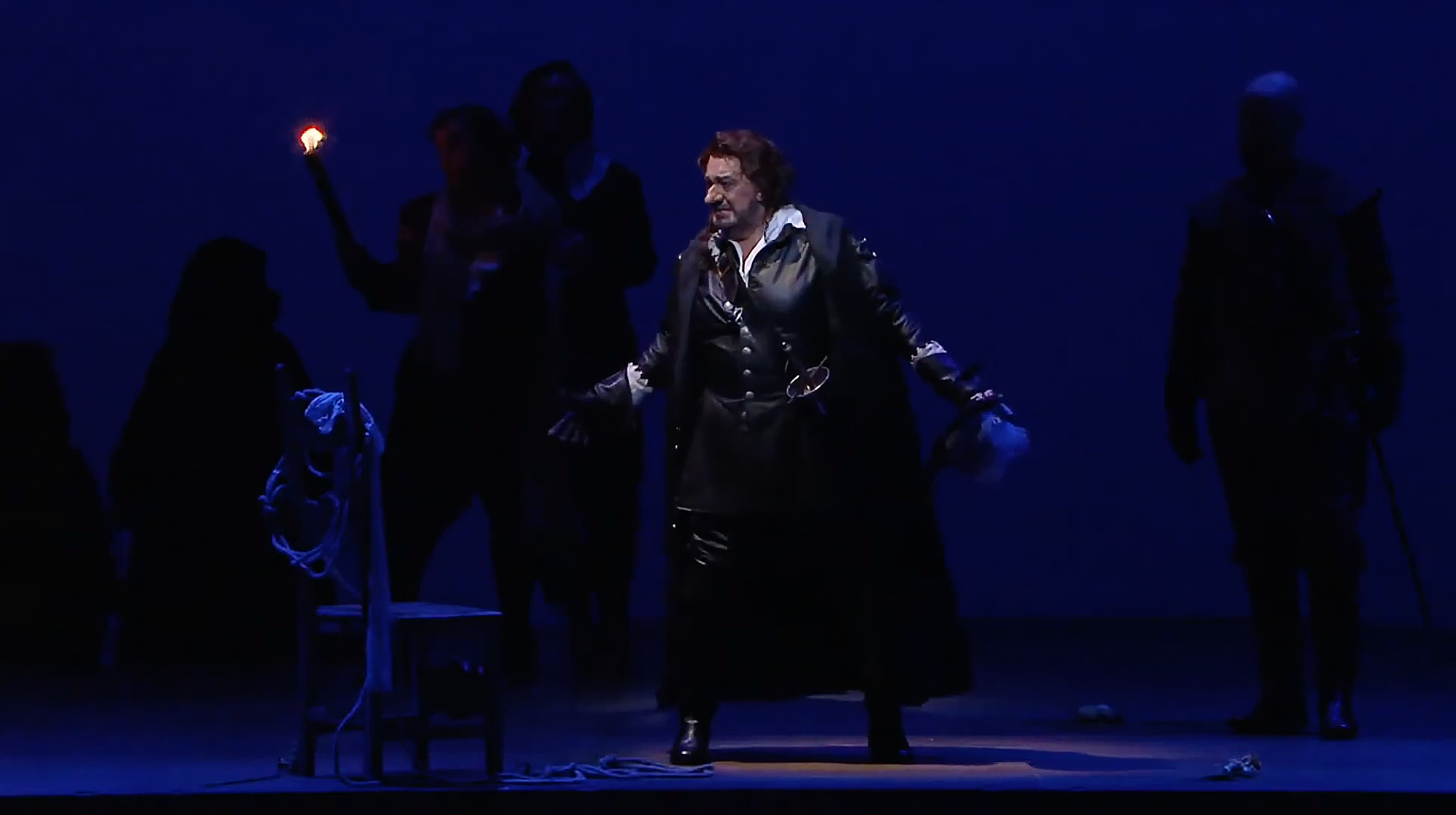 Film still of Plácido Domingo in Cyrano de Bergerac opera production at Teatro Real Madrid with cinematic blue stage lighting.