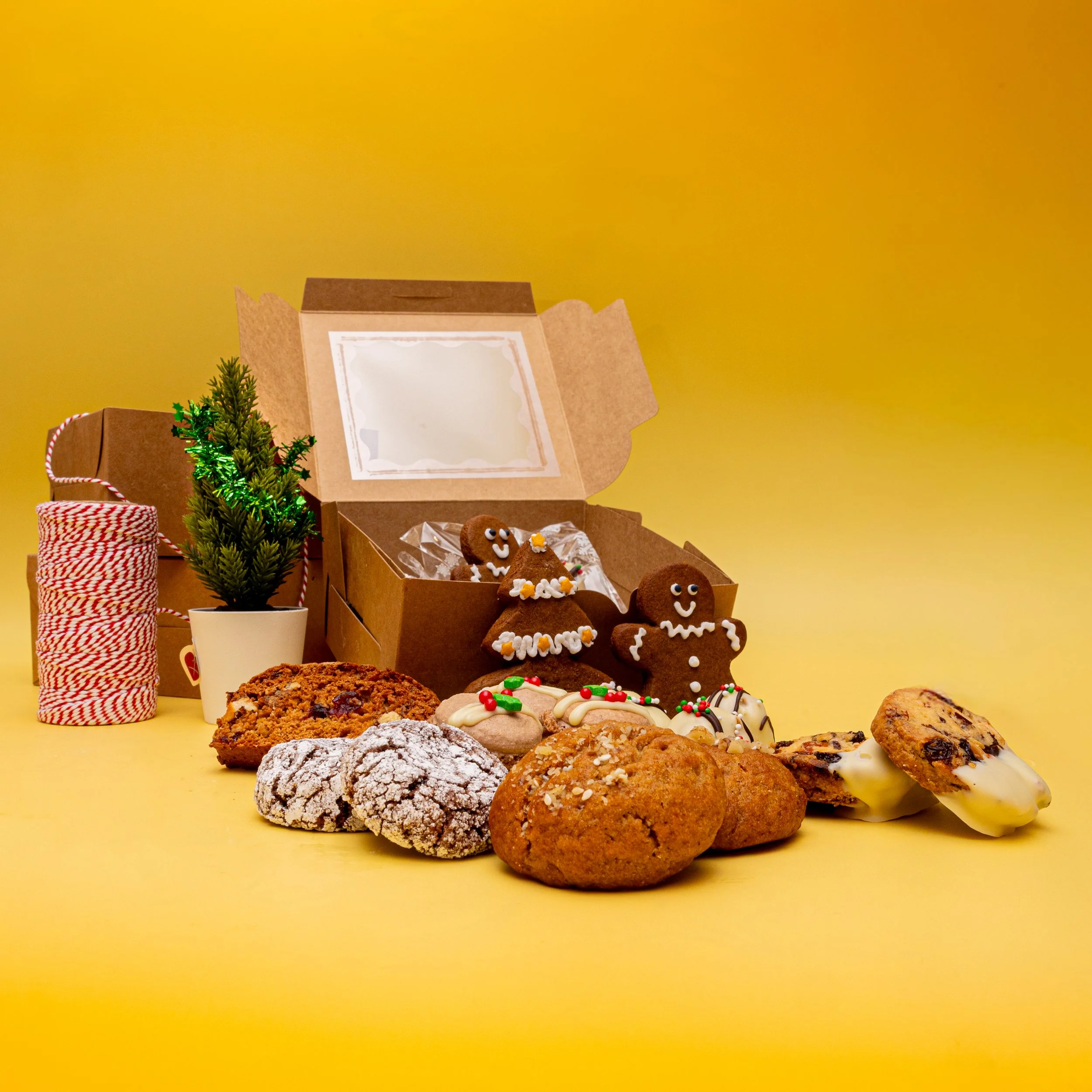Commercial Christmas food photography of festive bakery gift box with gingerbread men, assorted holiday cookies and seasonal props on yellow background
