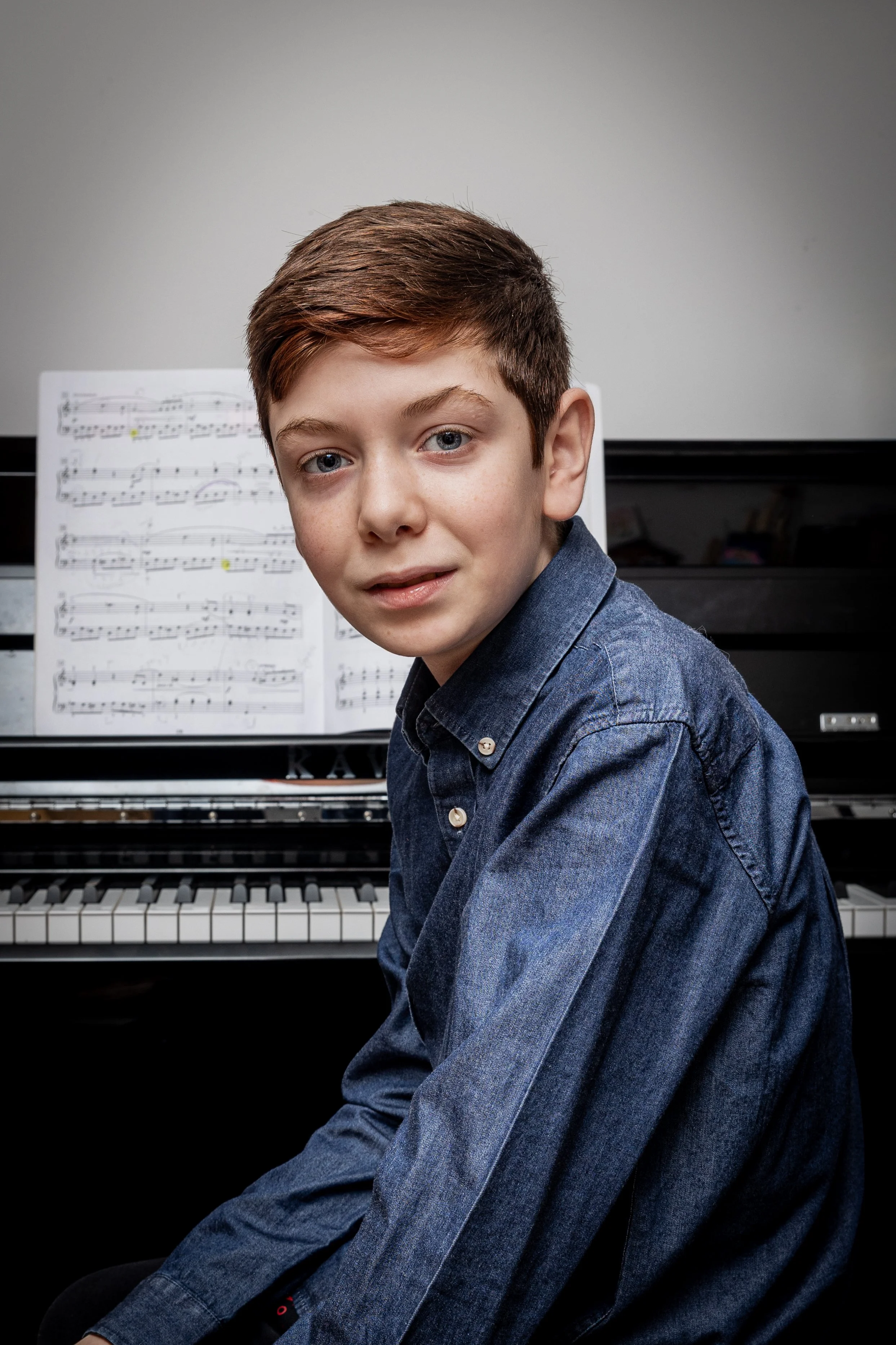 Portrait photography of young male pianist at upright piano with sheet music, professional studio portrait.
