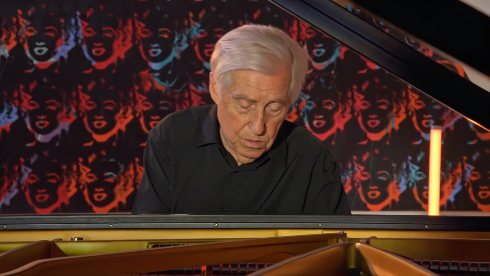 Film still of Joaquín Achúcarro, classical pianist performing at grand piano inside Guggenheim Bilbao with dramatic pop art backdrop.